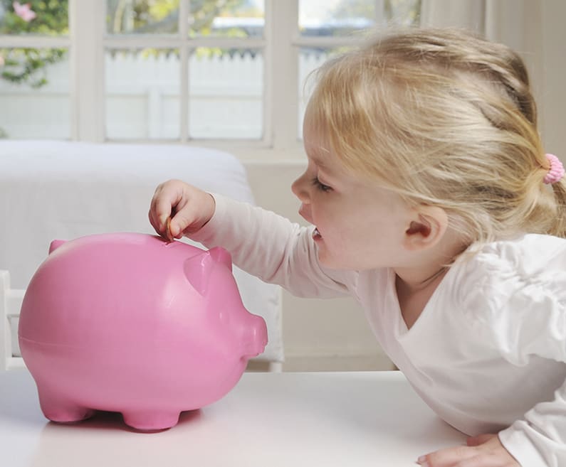 A girl puts a coin in a pink piggy bank.
