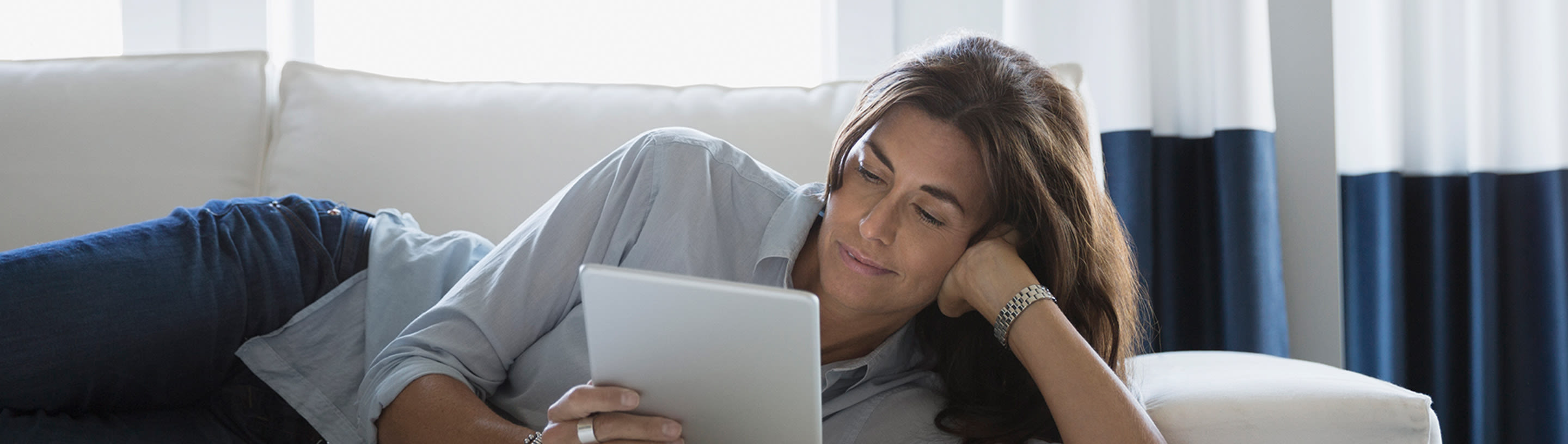 Woman lies on a couch with a tablet in her hands.