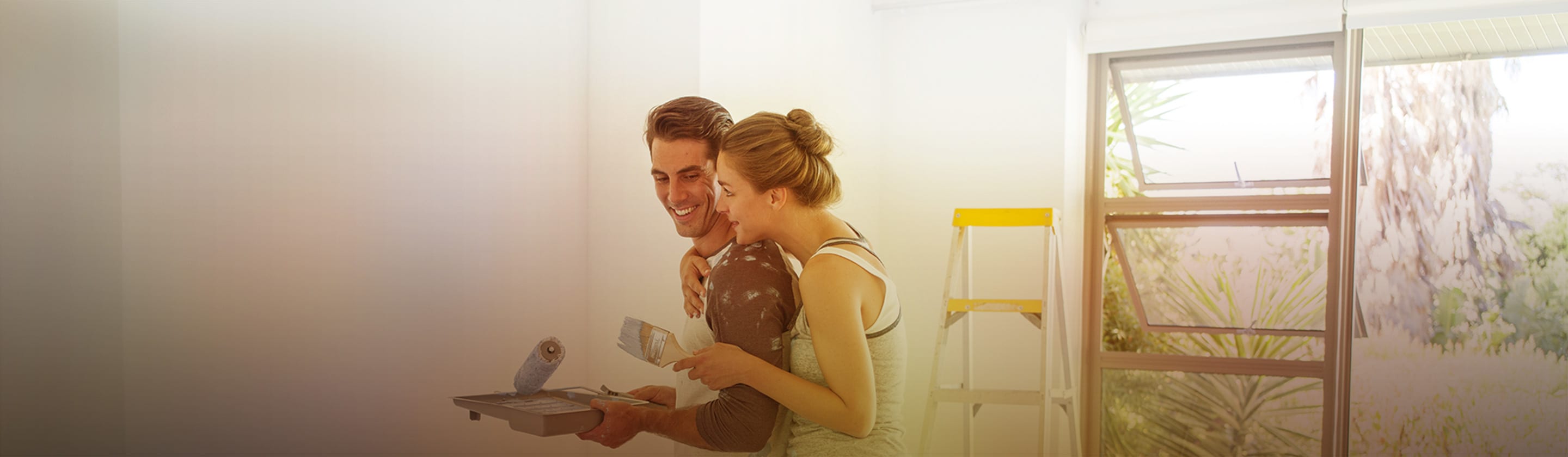 A young couple embracing each other holds wall painting supplies in their hands.