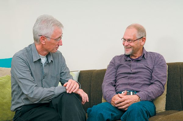 two caucasian men talking on couch