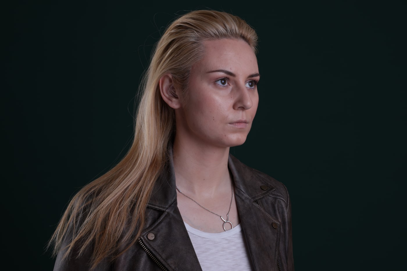 Low-key studio portrait in profile, blonde hair and a leather jacket, against deep green