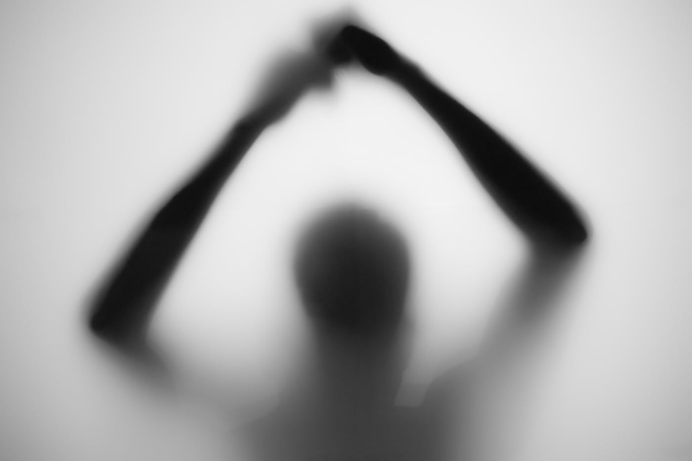 Blurred silhouette behind frosted glass, arms raised overhead into a triangle