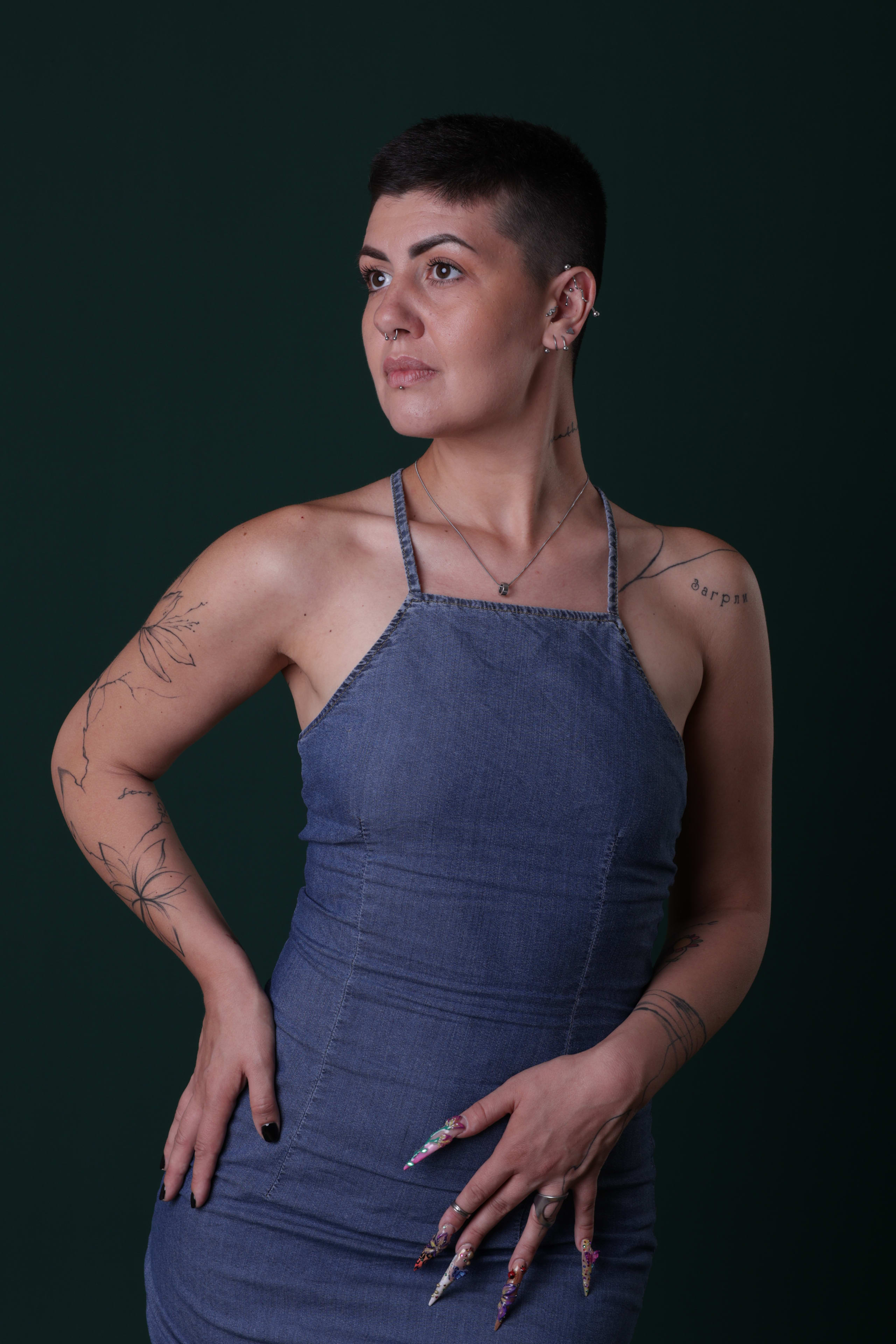 Studio portrait against a deep green backdrop, hand on hip, denim slip dress, gaze off camera