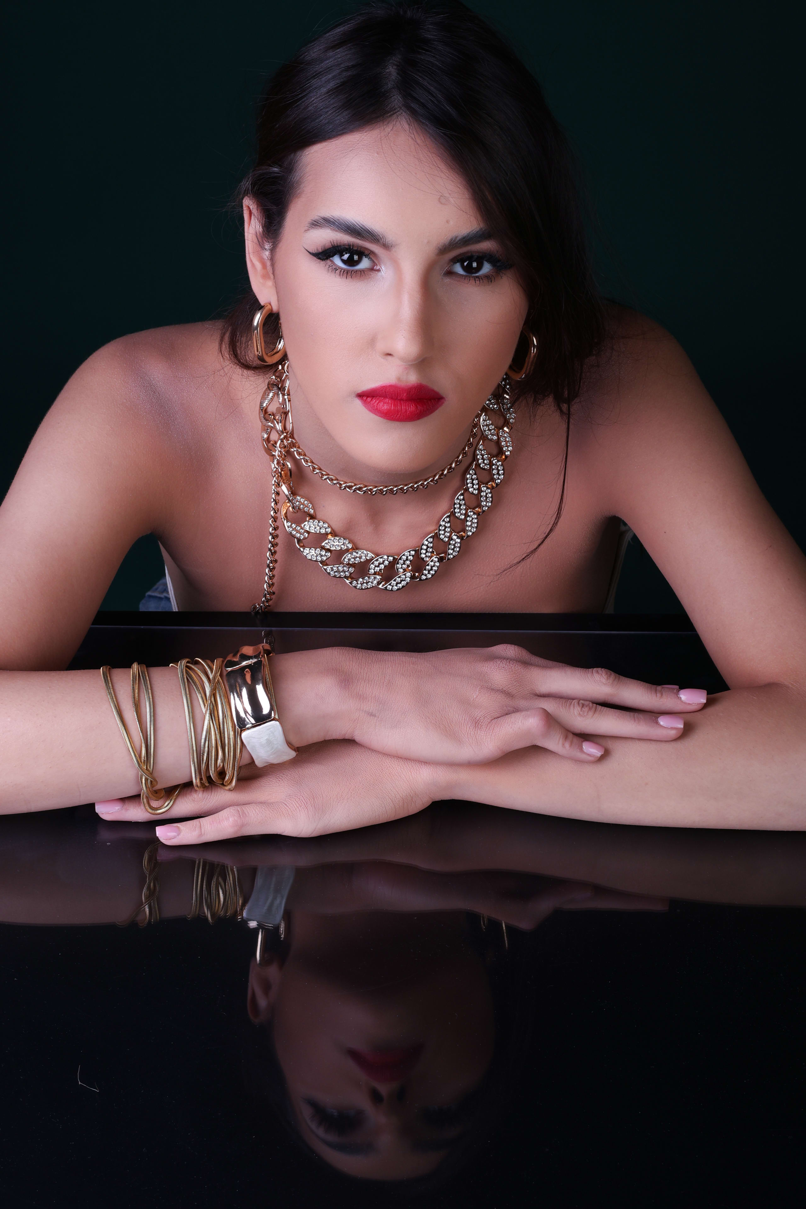 Arms folded on the mirror, intense gaze to camera, a chunky gold chain-link necklace and cuff