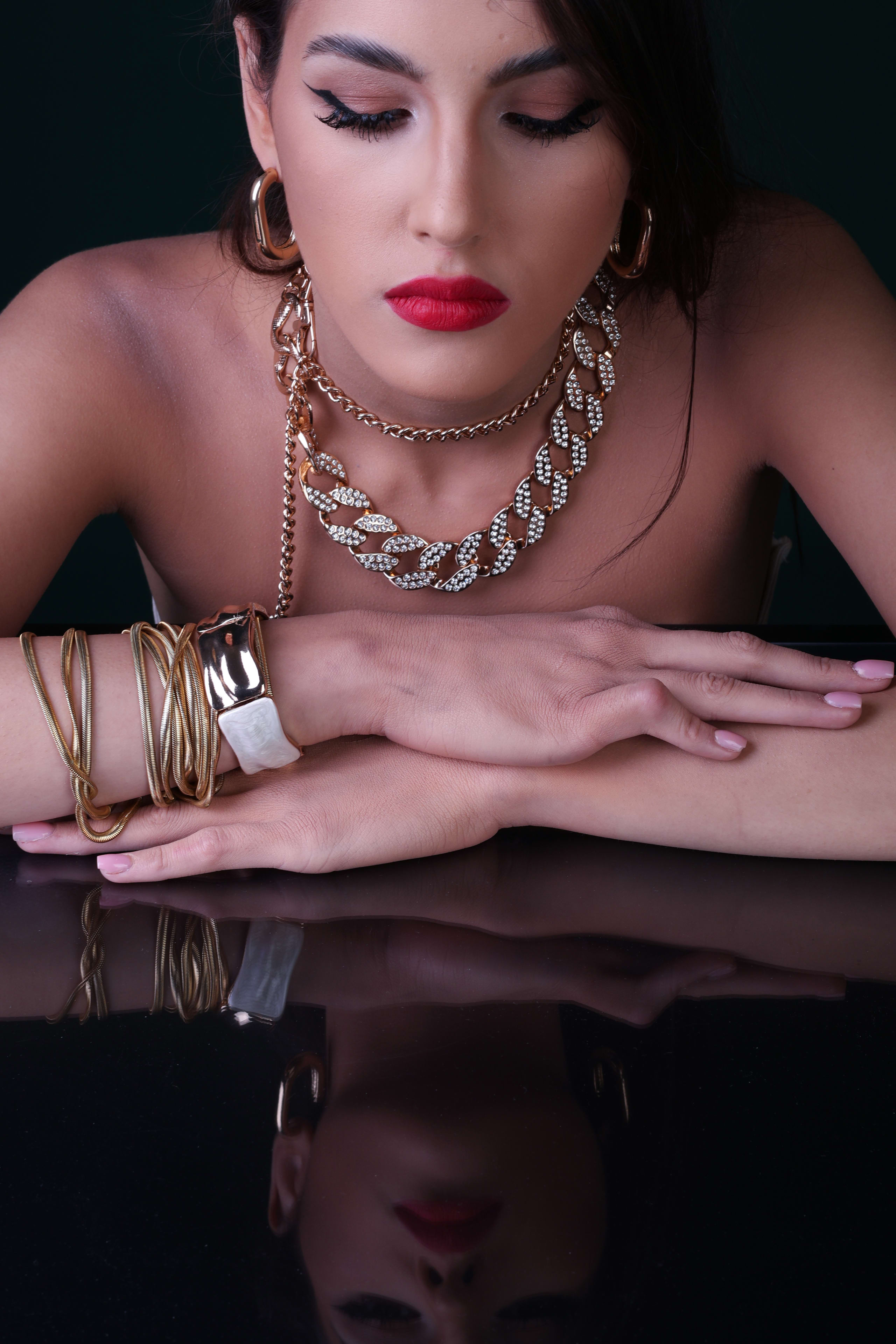 Looking down at a heavy gold chain-link necklace and gold cuff, mirrored on the black glass
