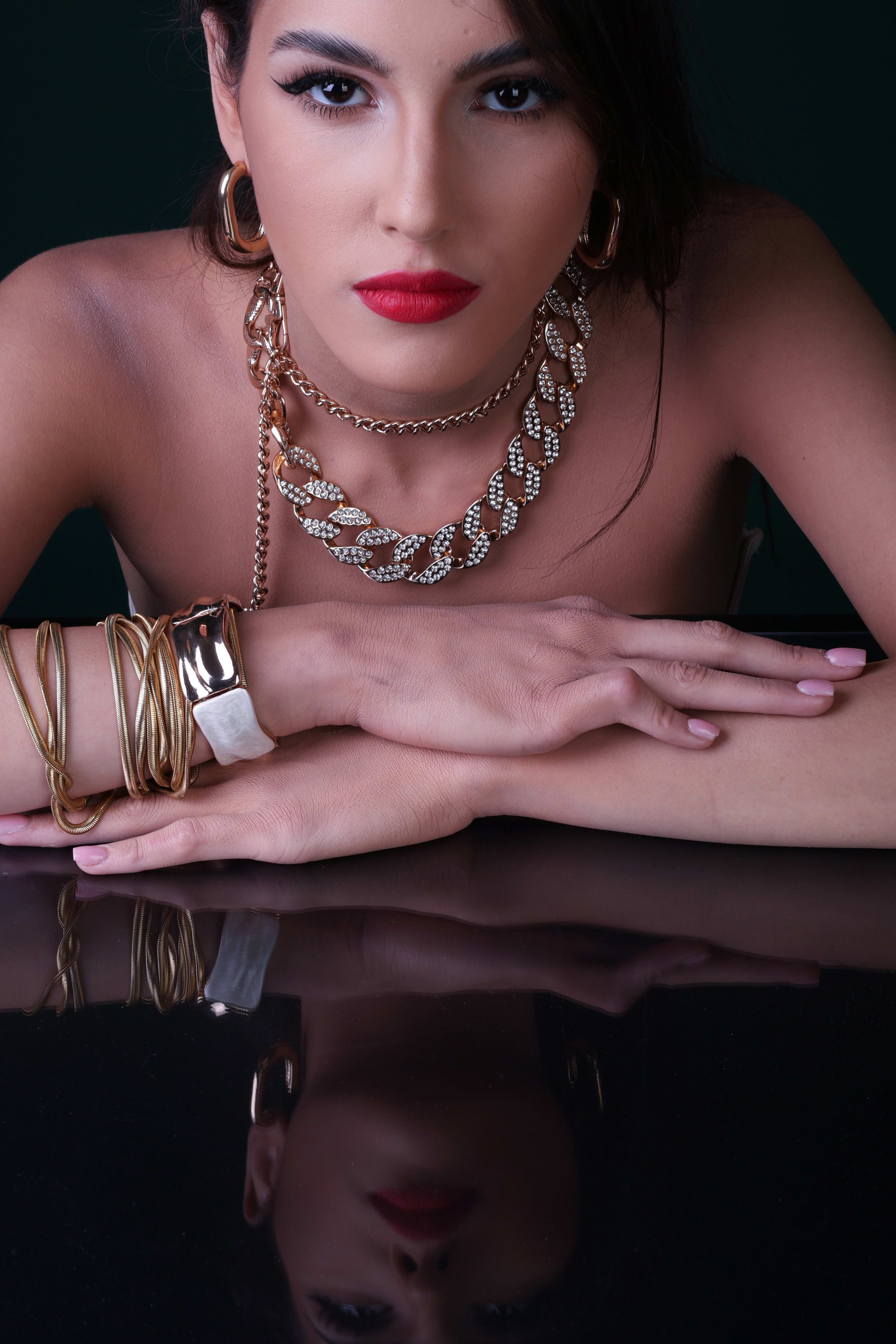 Chin on folded hands with a steady gaze, gold Cuban-link chain, reflected on black glass