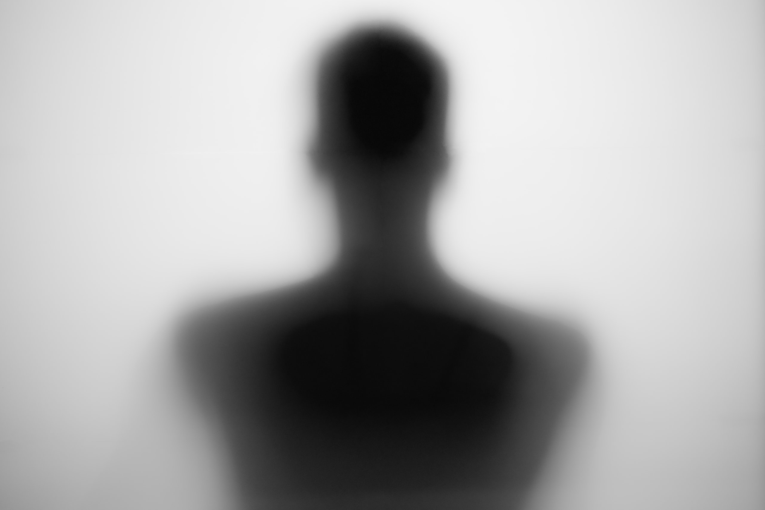Soft silhouette of a head and shoulders seen from behind, behind frosted glass