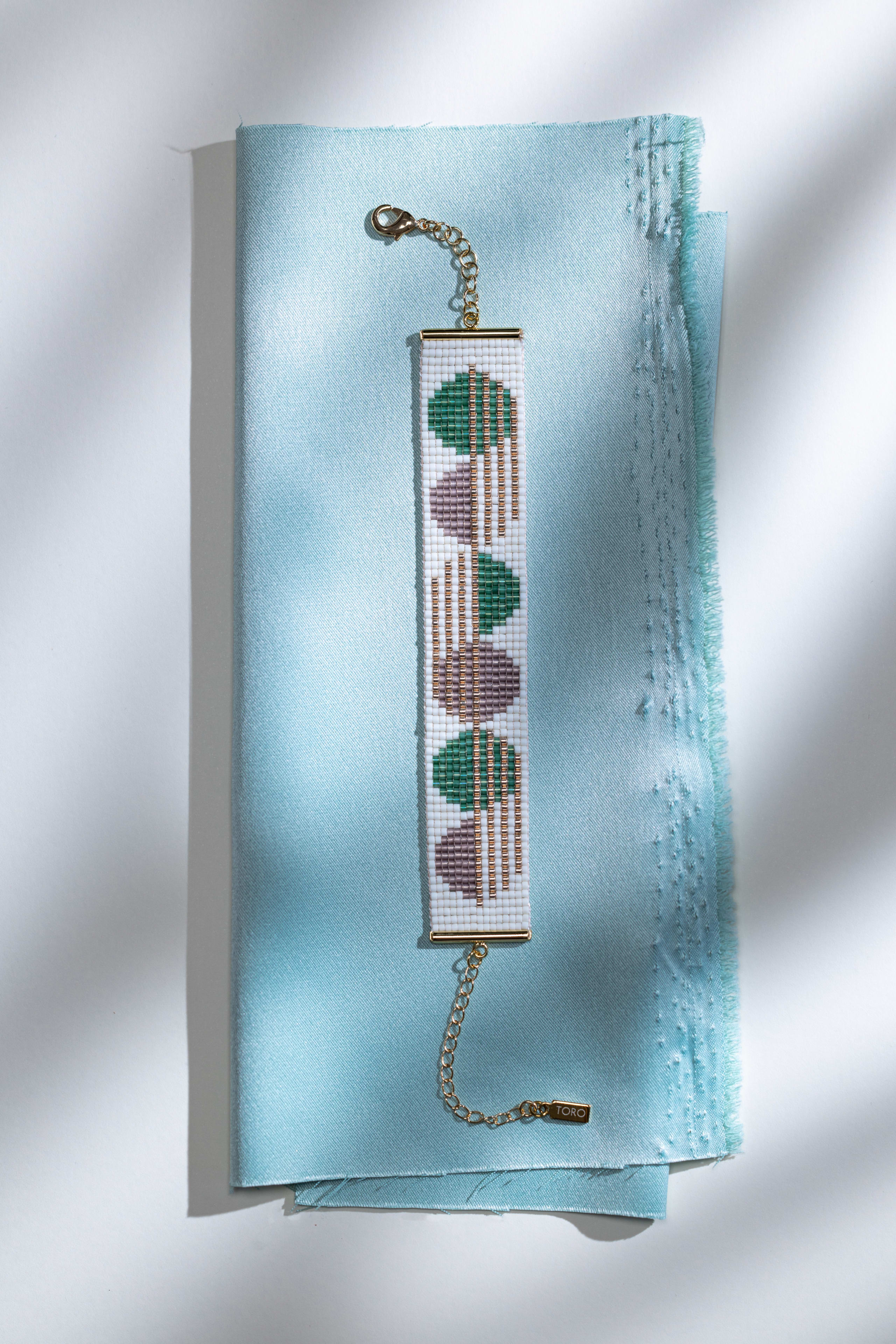 A cuff patterned in green and mauve half-circles on folded mint silk, soft diagonal light across the frame