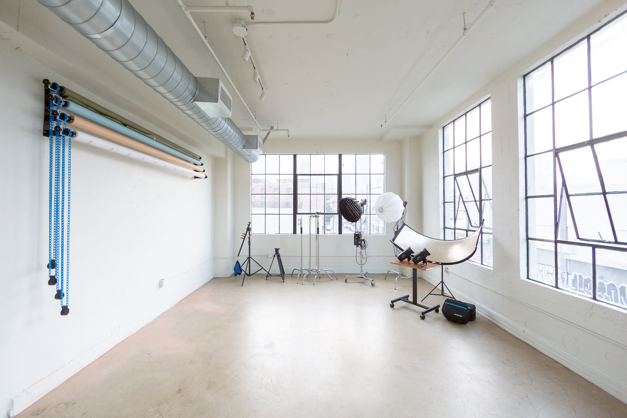 A spacious studio with large windows, equipped with lighting gear and a backdrop, is set up for an apparel photoshoot.