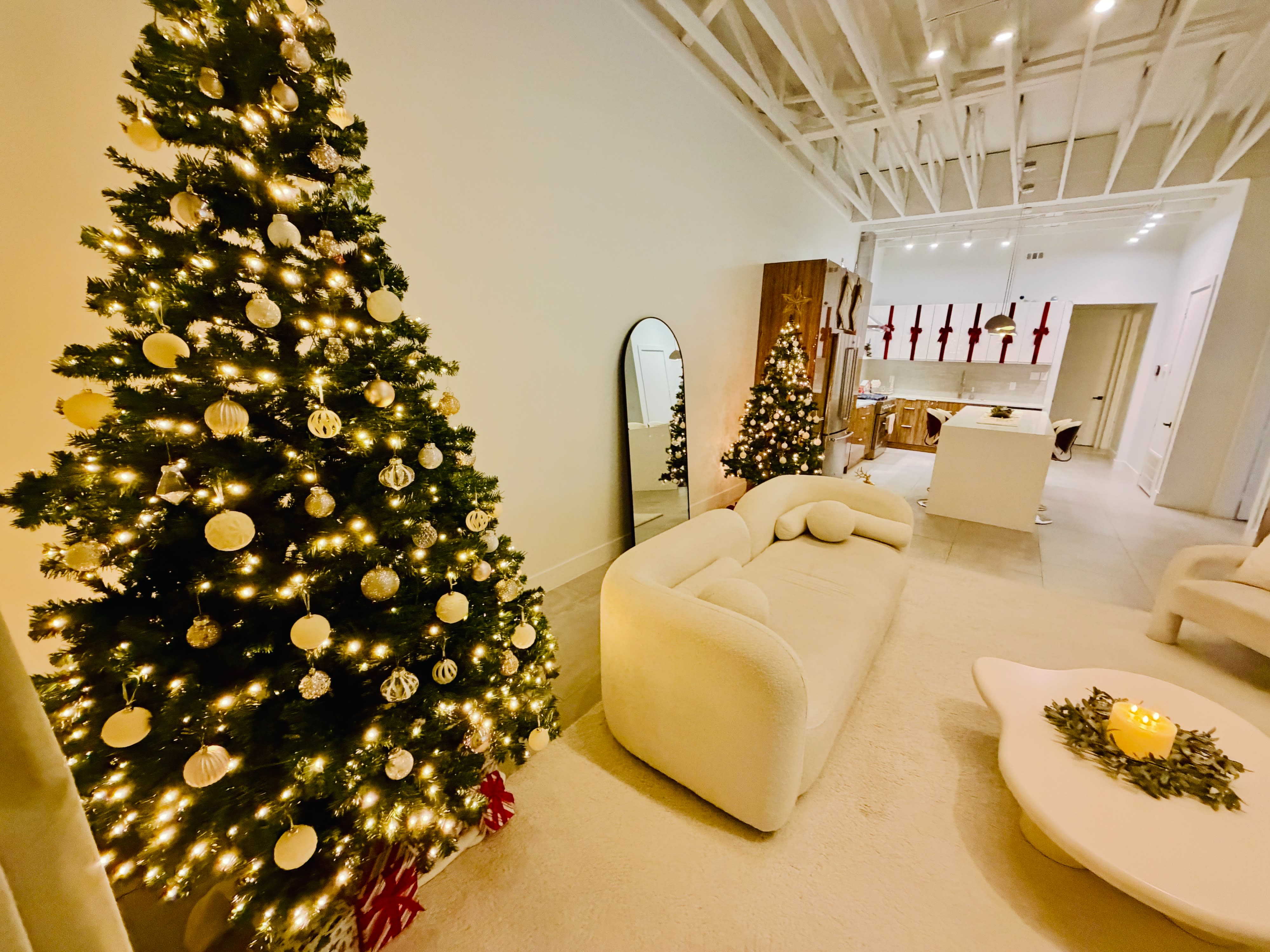 A model poses on a white couch in lingerie, surrounded by festive decorations and a Christmas tree.