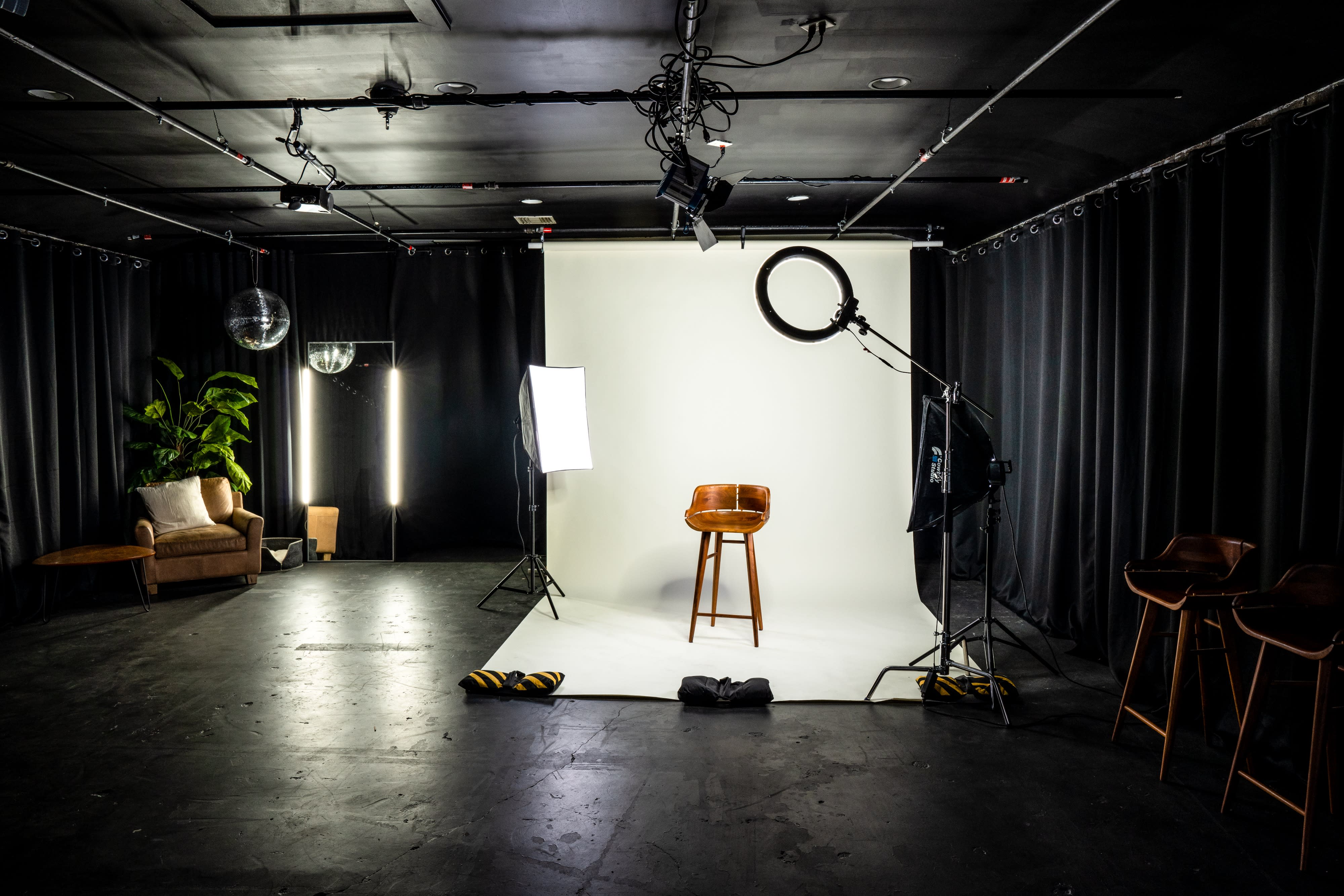 A video shoot is in progress with a person seated under bright lights while crew members operate cameras and equipment.