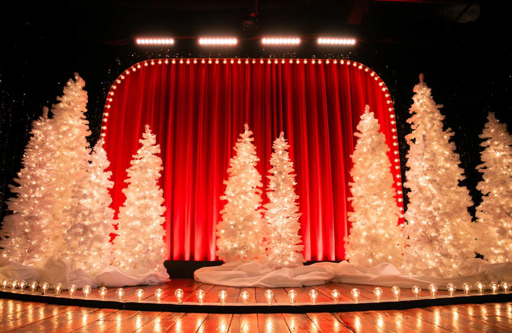 A performer in a red leather jacket strikes a pose while holding a microphone on a glittering stage backdrop.