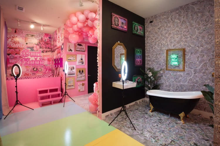 A woman in a shimmering teal dress poses playfully beside a bathtub surrounded by scattered dollar bills.