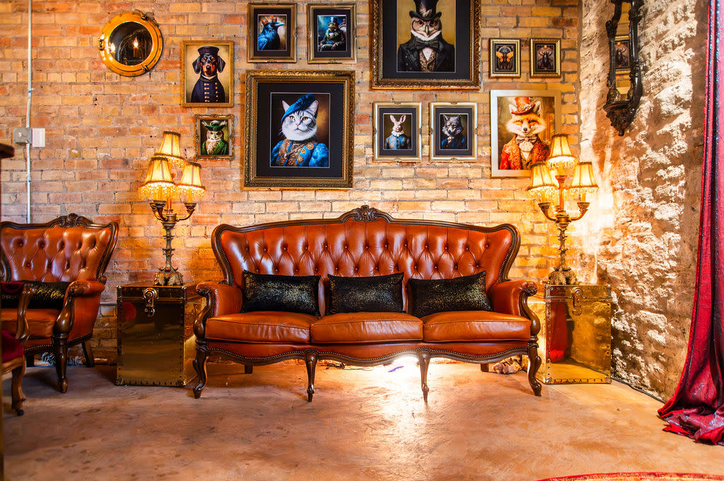 The scene features a cozy room with a vintage sofa and a wall adorned with framed portraits of animals dressed in formal attire, creating a whimsical atmosphere.
