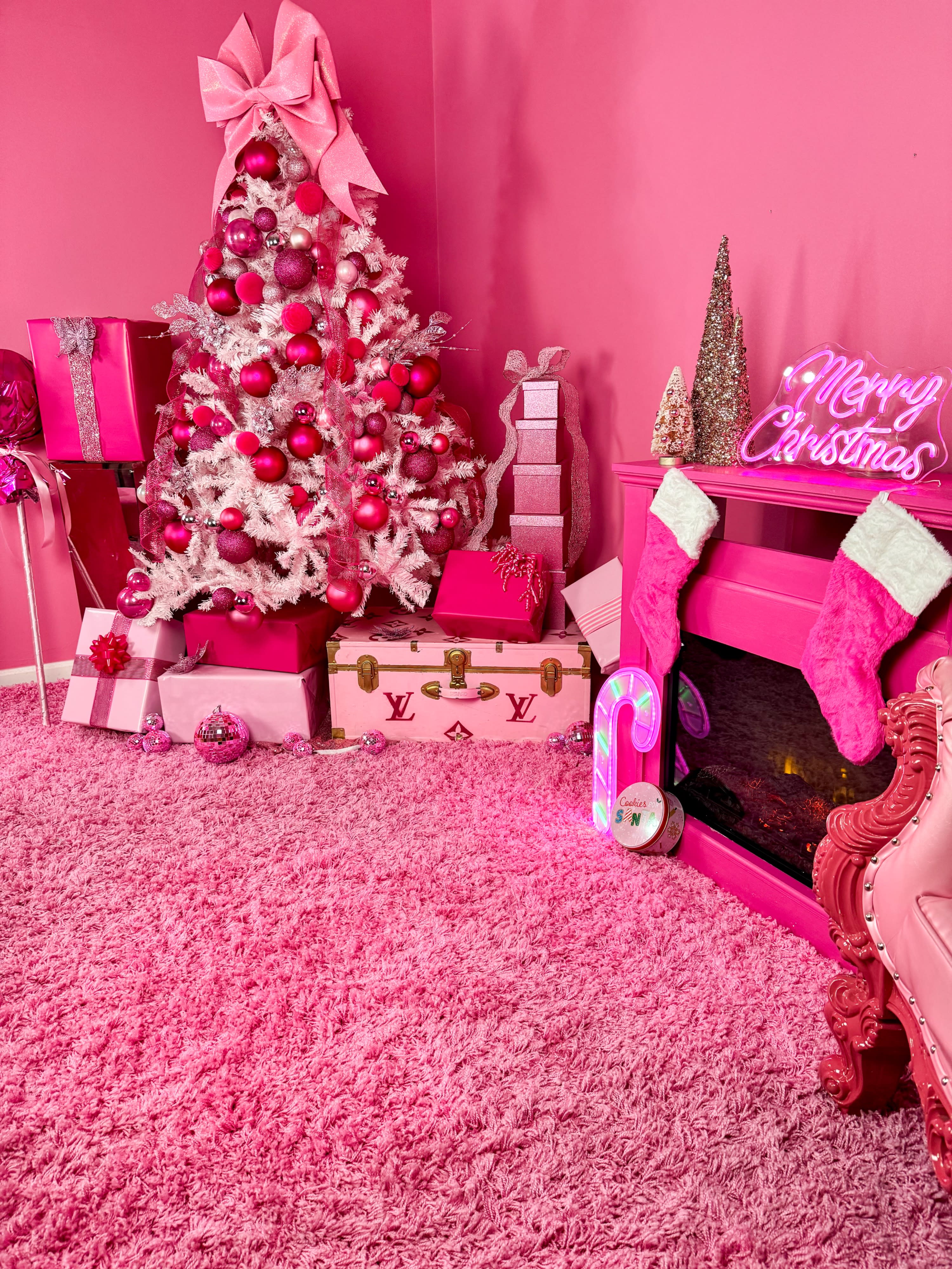 A brightly colored pink room set up for a photoshoot, featuring a vanity, a plush chair, and neon signs.