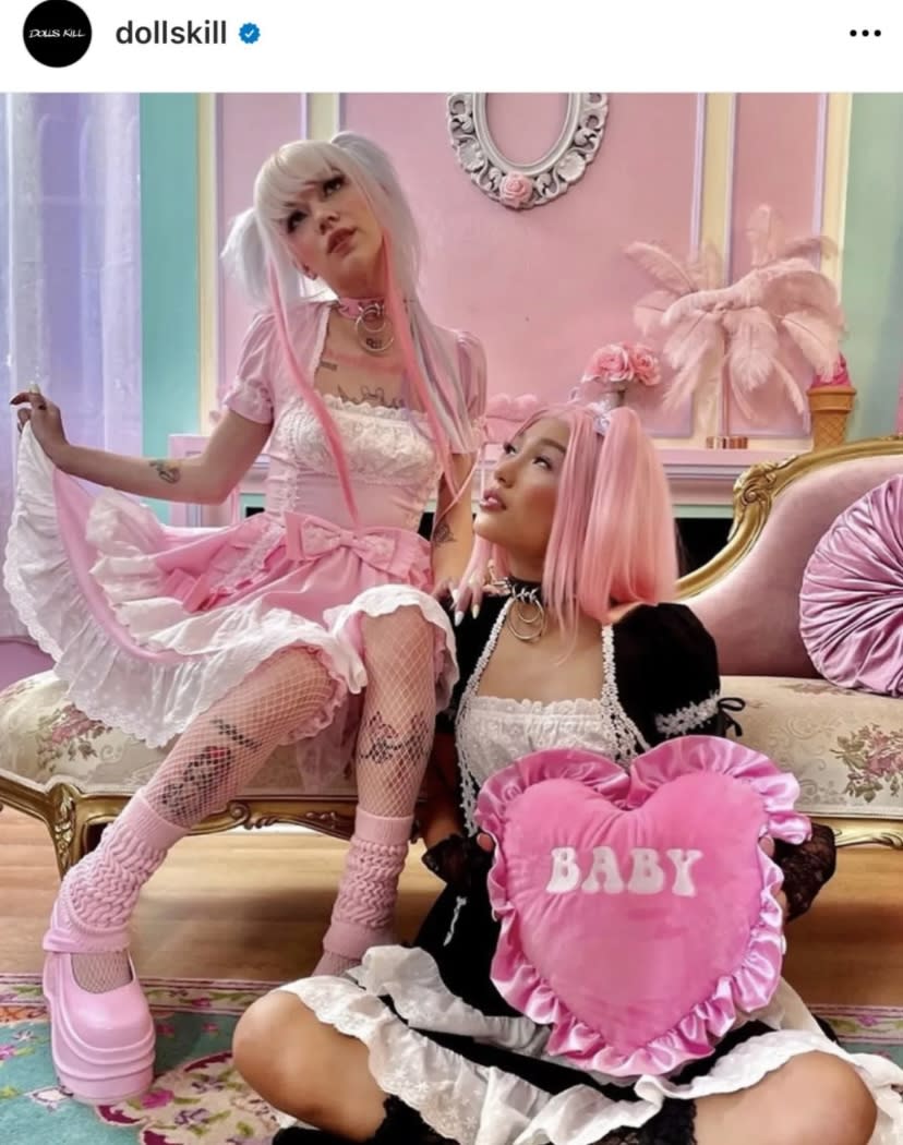 A group of five girls poses together in colorful dresses on a couch in a brightly decorated room during a photoshoot.