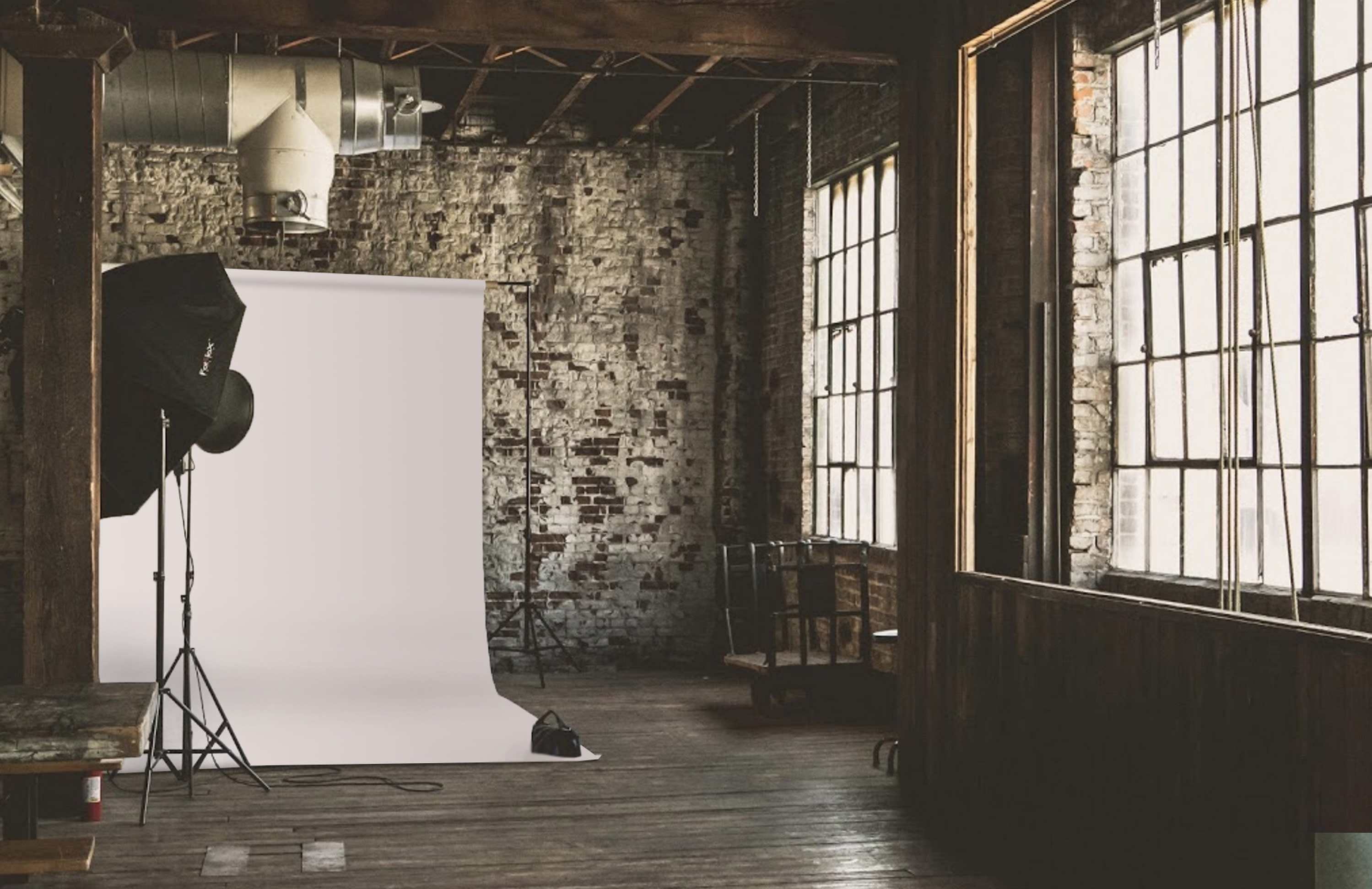 A photographer captures a model holding a smartphone in a studio with a rustic brick wall.