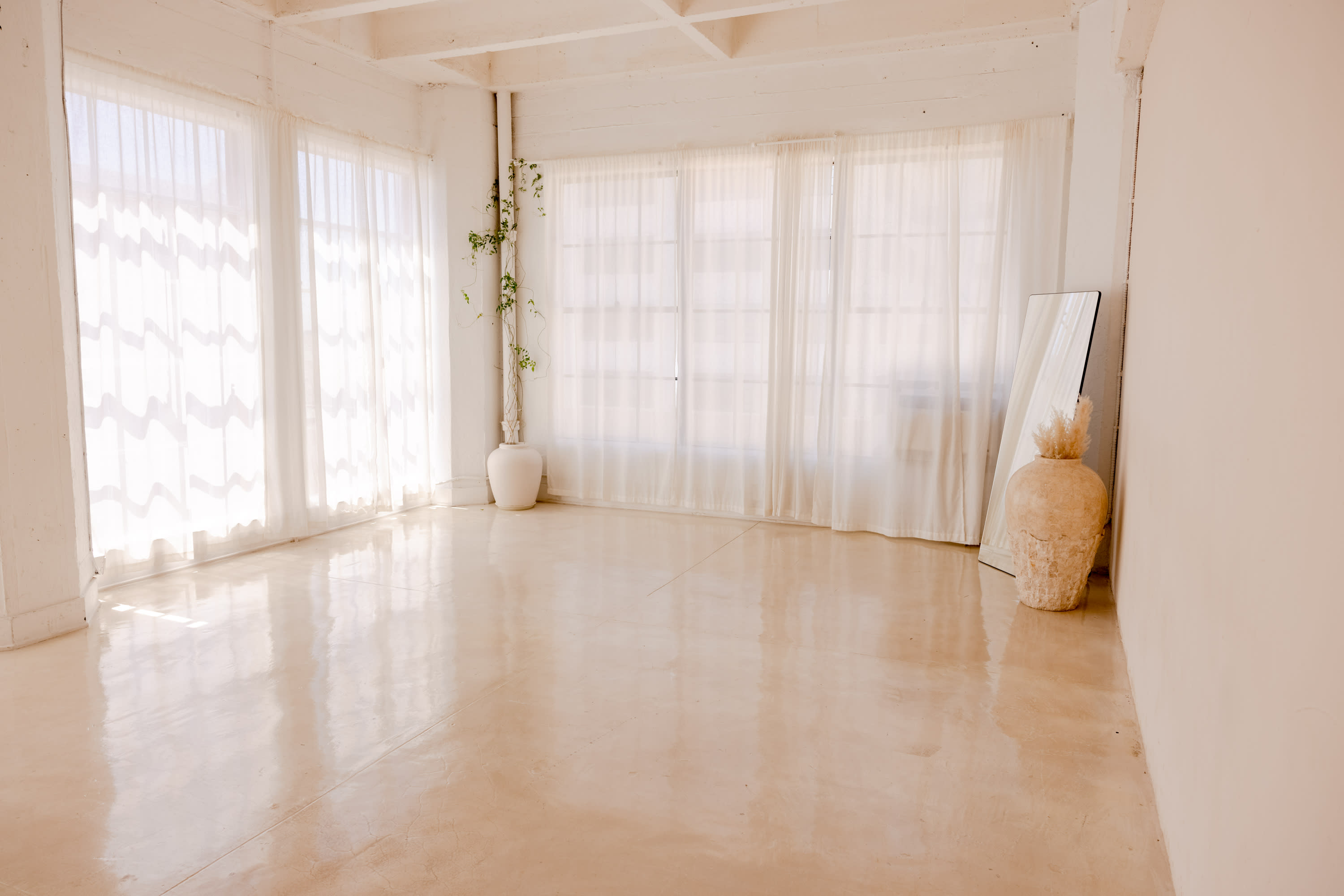 A couple poses closely together in a sunlit room, gazing into each other's eyes while holding hands near a large window.