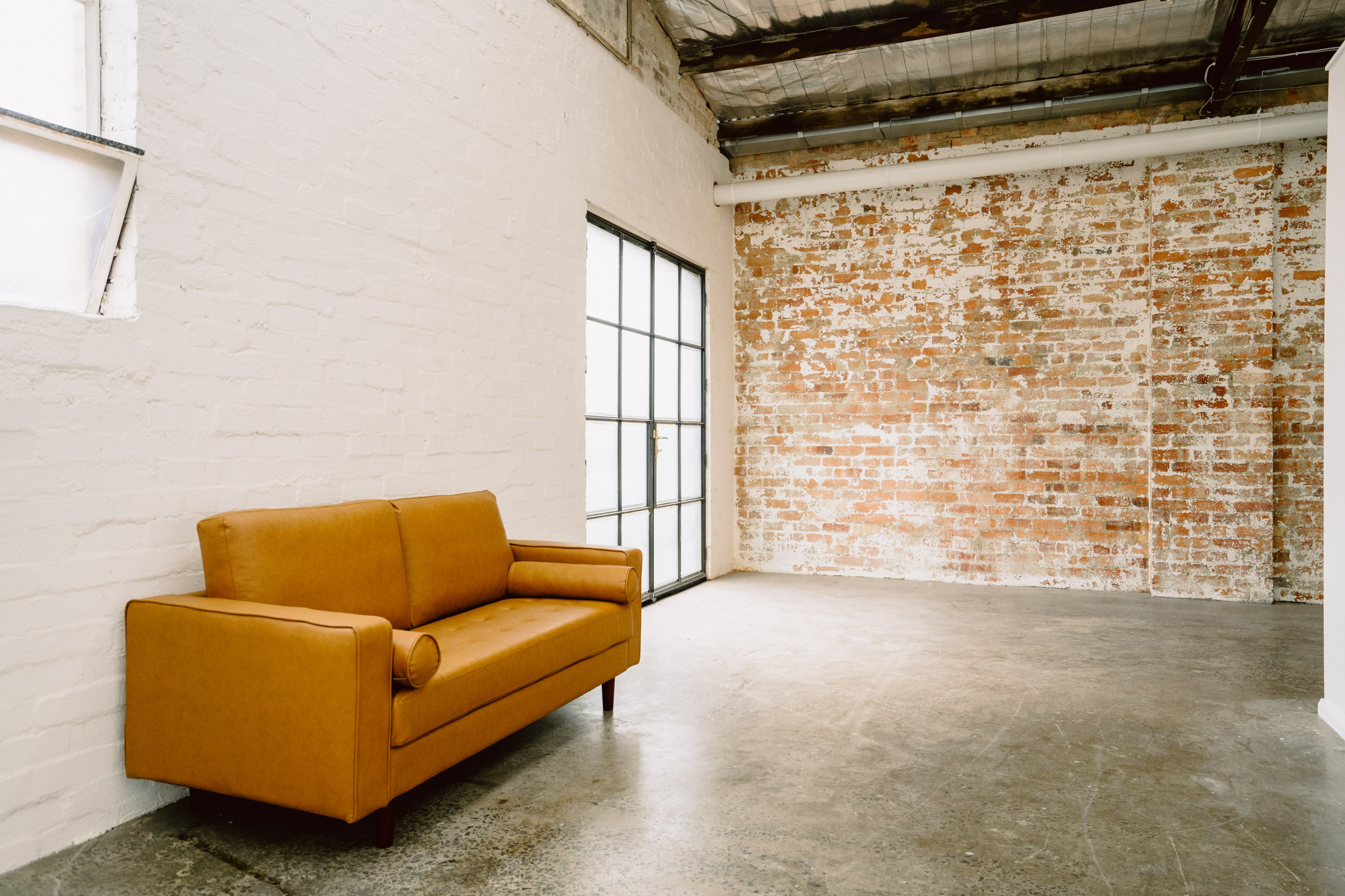 A person stands in a spacious studio space with exposed brick walls, surrounded by photography equipment, including lights and a backdrop.