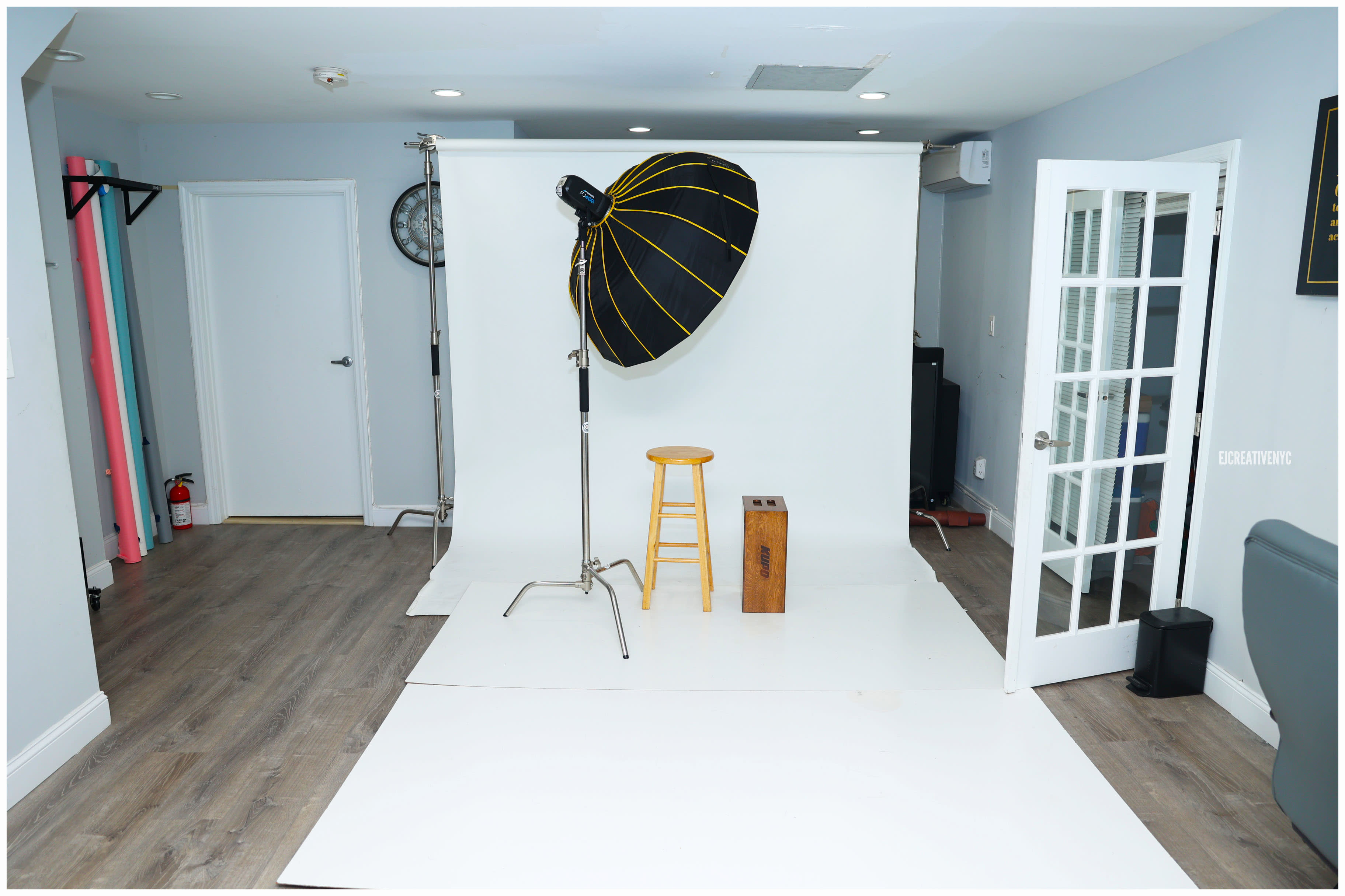 A man in a black shirt sits on a wooden box and tosses fake dollar bills into the air during a birthday photo shoot.