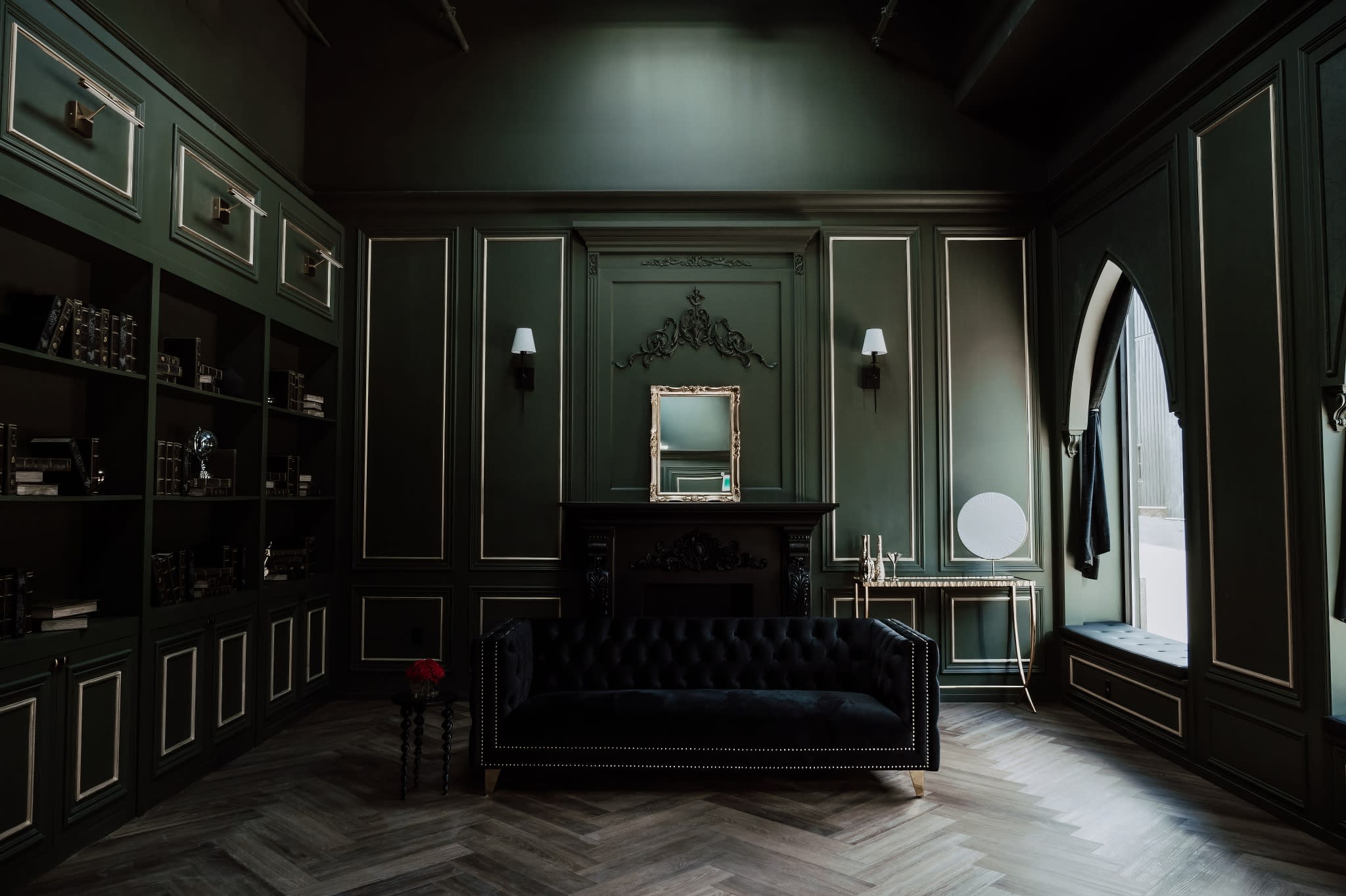 A model poses confidently on a plush black sofa in a stylized indoor setting.