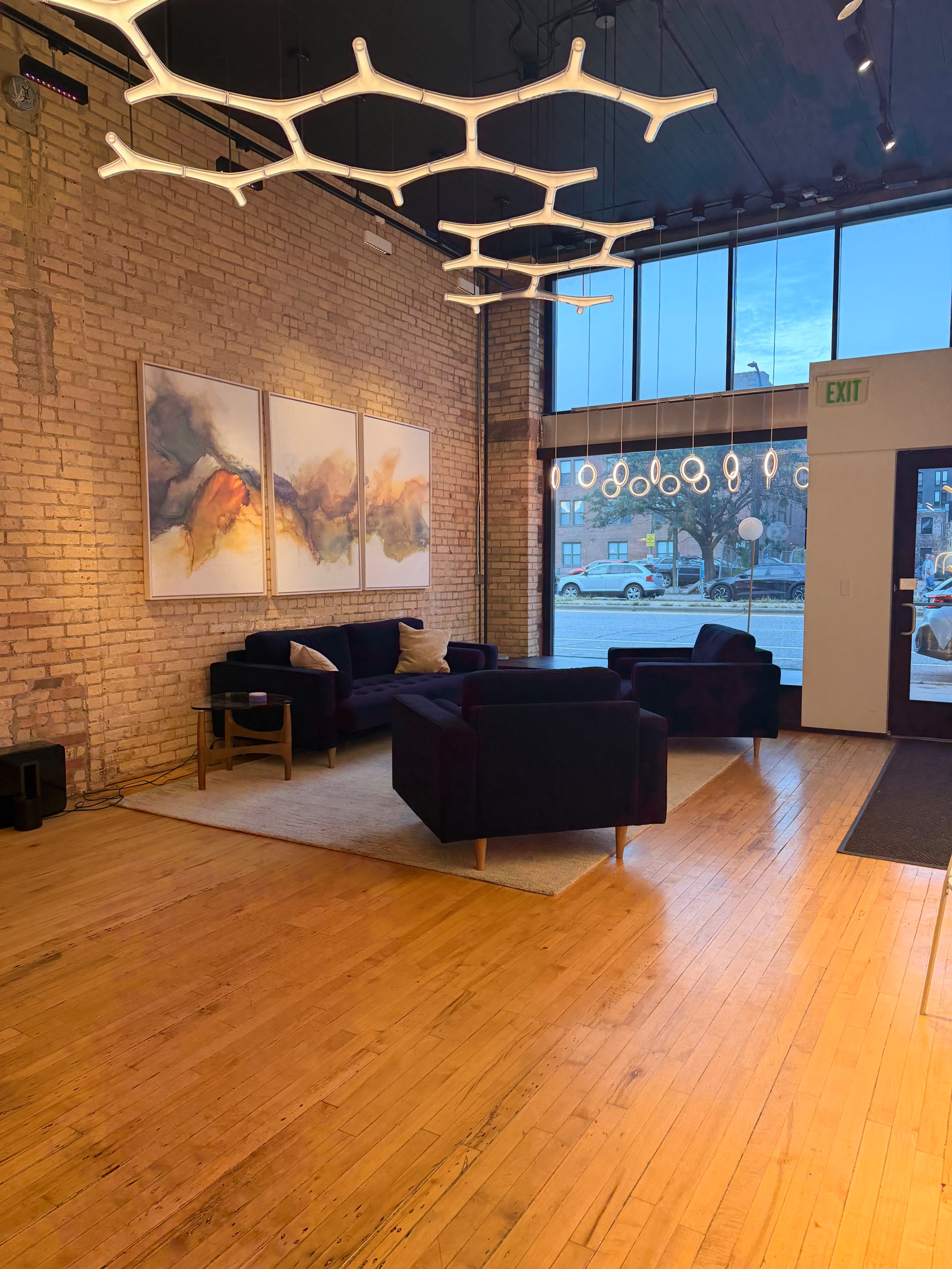 The image shows a modern, minimalist living space with a kitchen area, a seating arrangement, and a gallery-style wall.