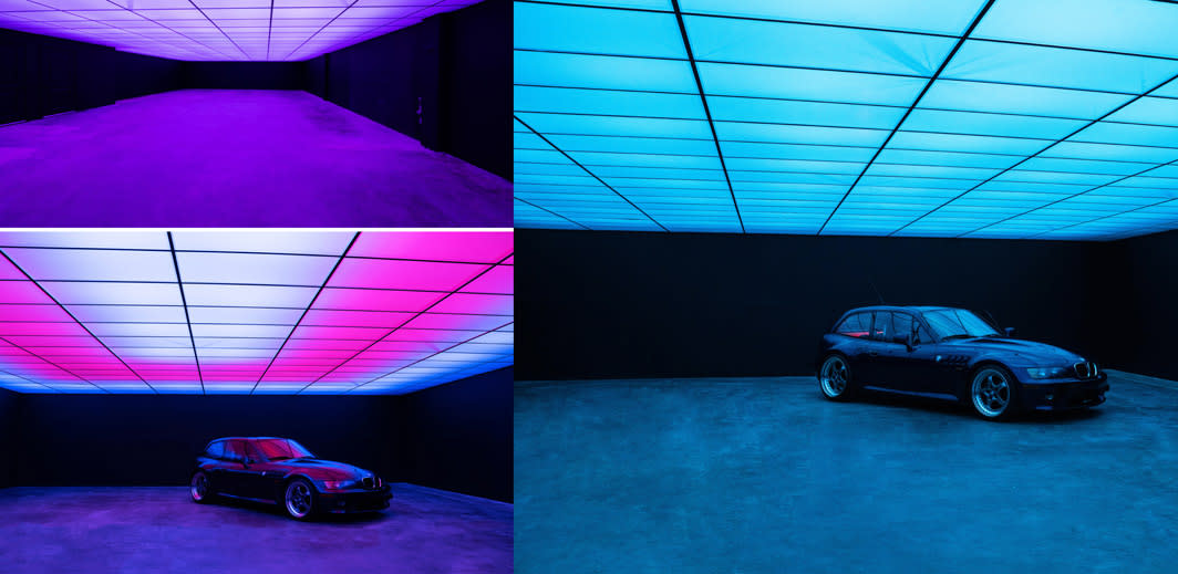 A model poses in a dark space wearing a hoodie, with a brightly lit ceiling creating a dramatic backdrop.