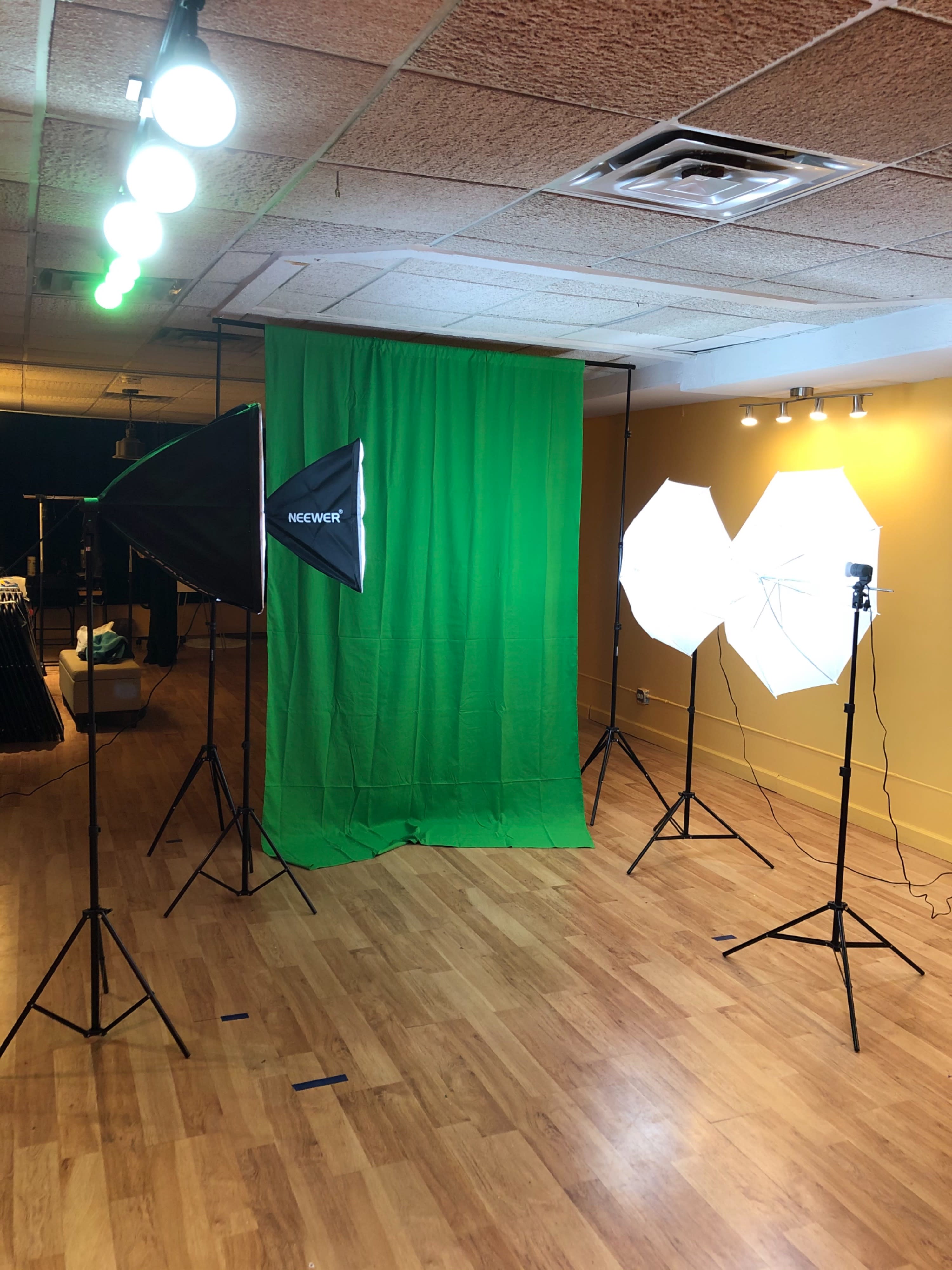 A camera operator films two women in a brightly lit studio with colorful stage lights during a video shoot.