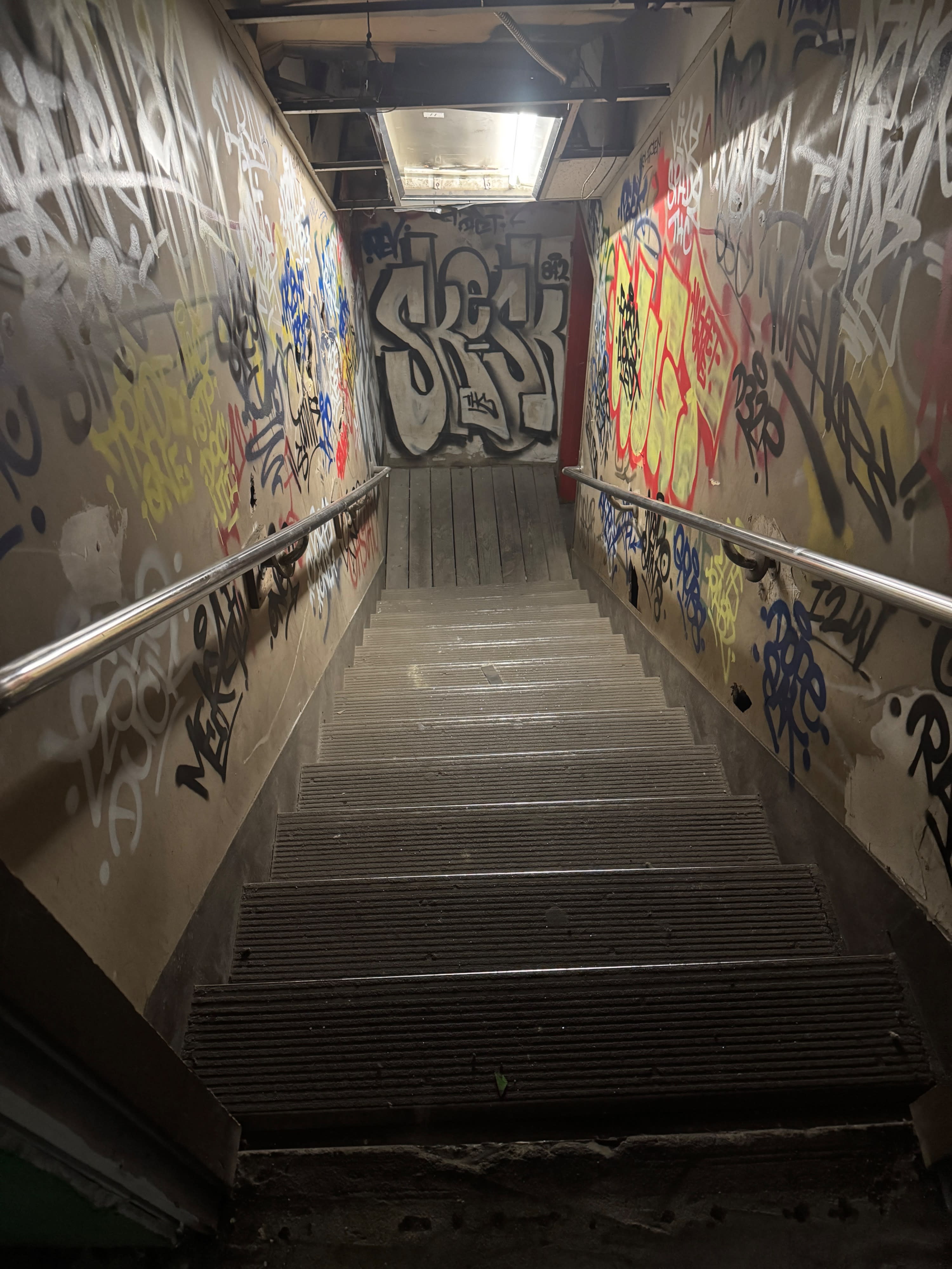 A person walks through a dimly lit, empty industrial space with large windows casting shadows on the floor.