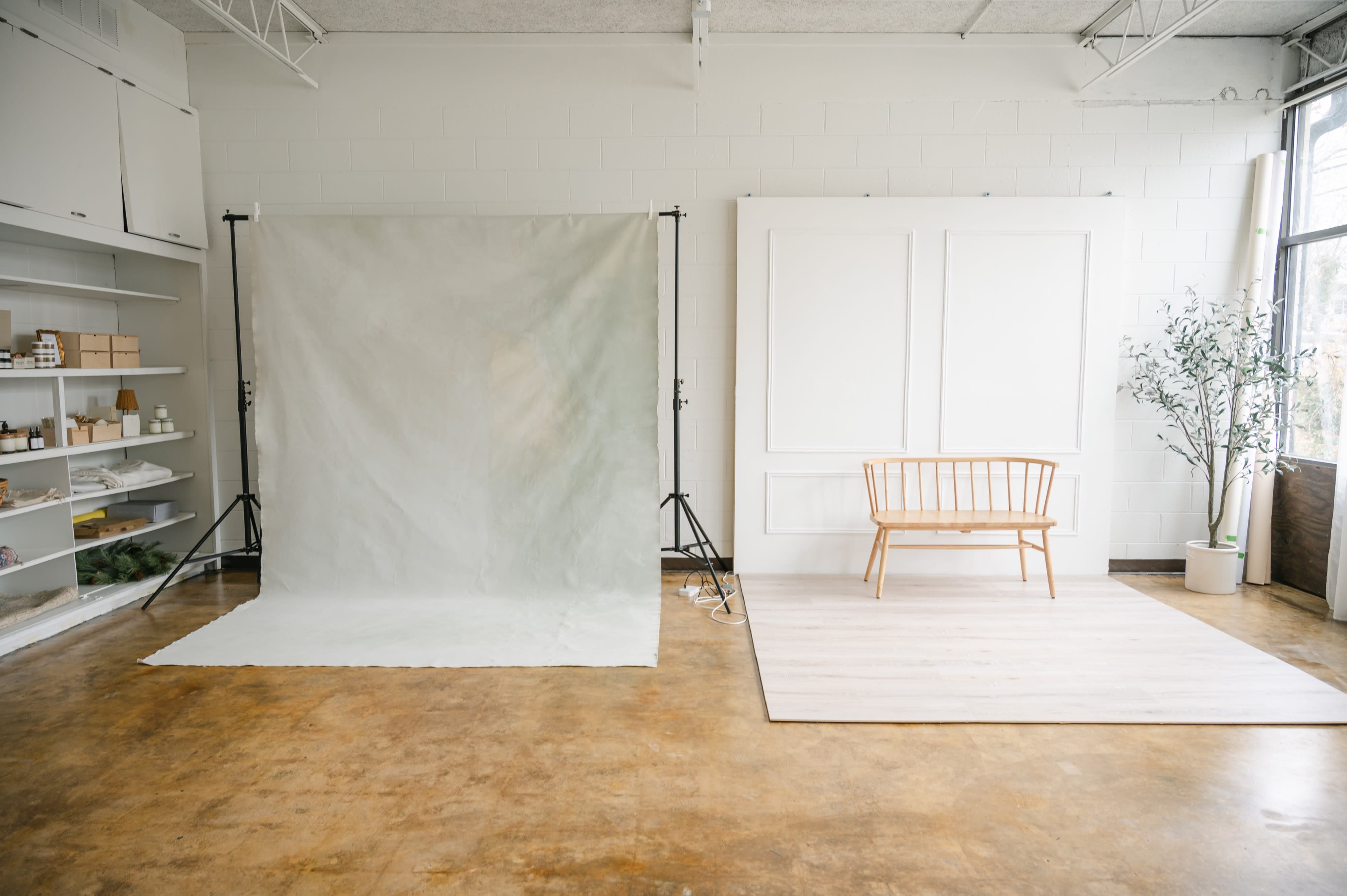 A cozy studio setting features a minimalist seating area with two wooden armchairs, a sofa, and a coffee table surrounded by decorative elements.