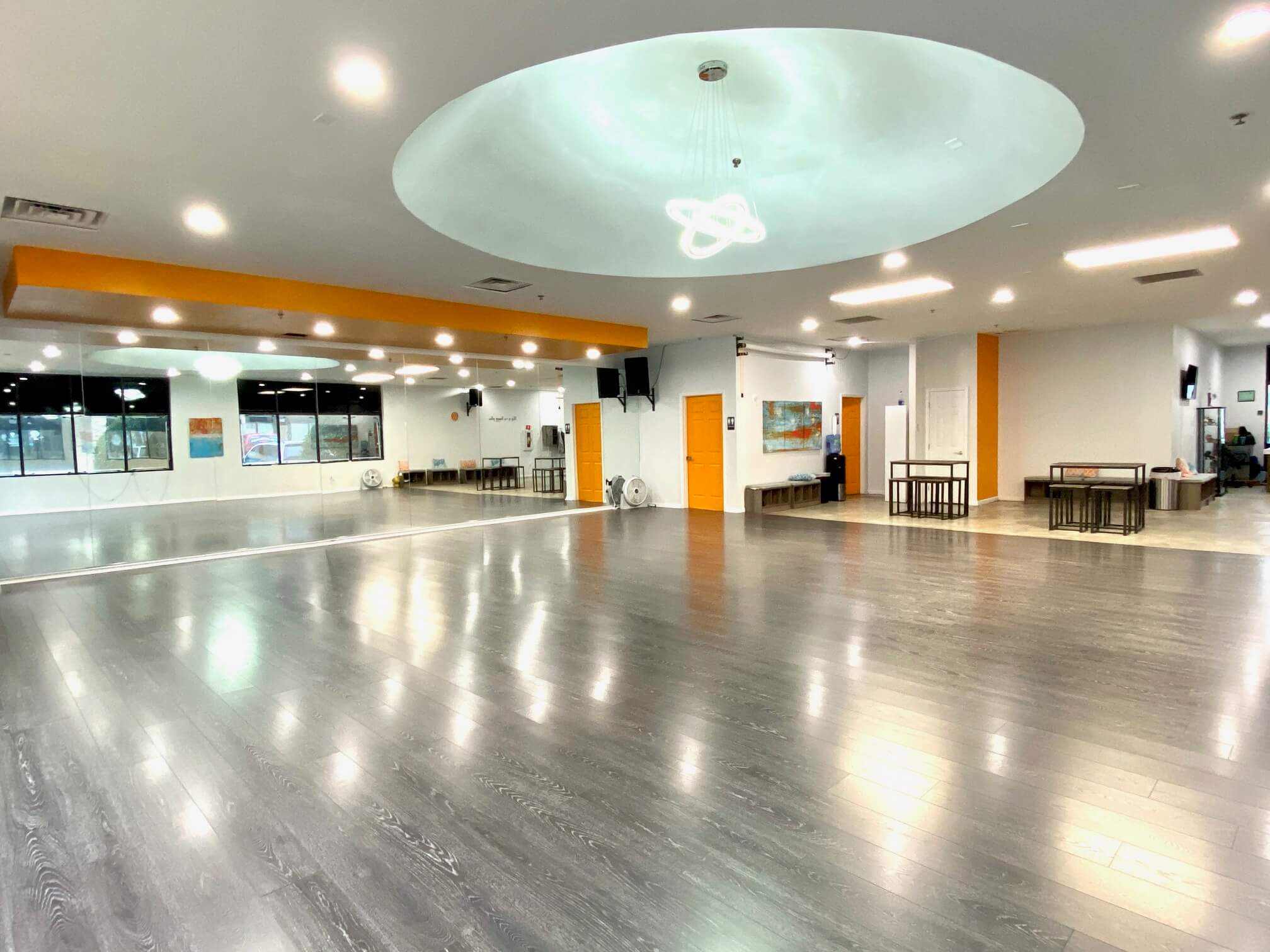A group of individuals performs yoga poses in a studio setting with large windows and wooden flooring.