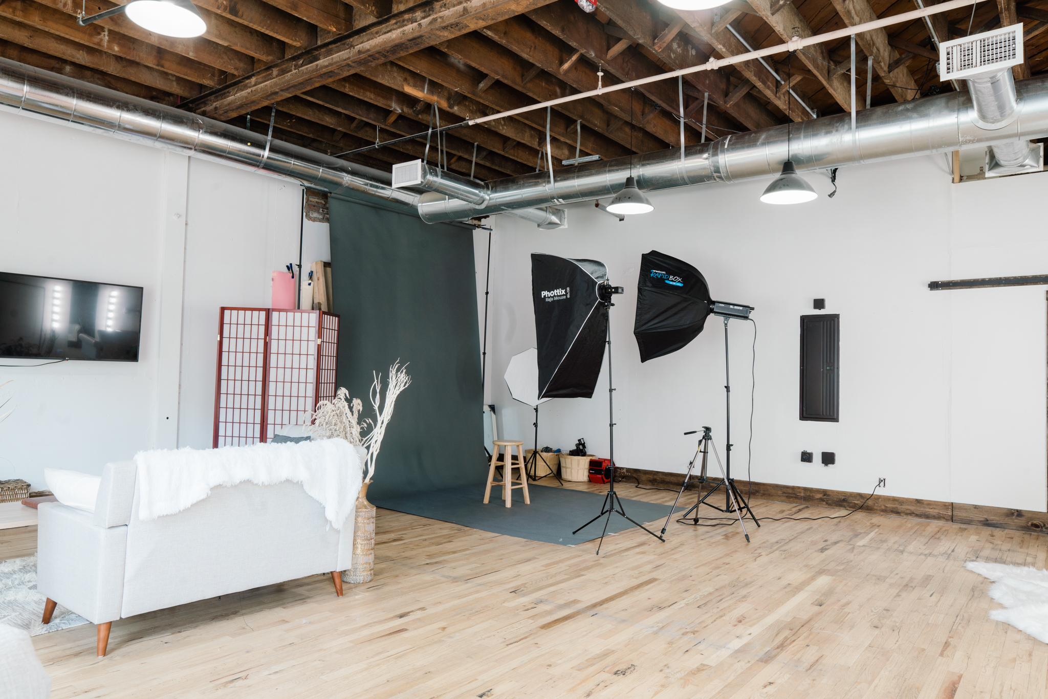 Two women are seated on a couch during a video shoot, surrounded by cameras and lighting equipment in a studio setting.