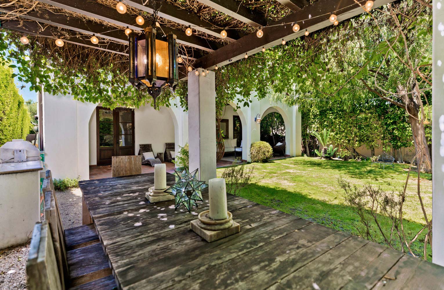 A long outdoor dining table is elegantly set with candles, flowers, and dinnerware, ready for a birthday dinner celebration.