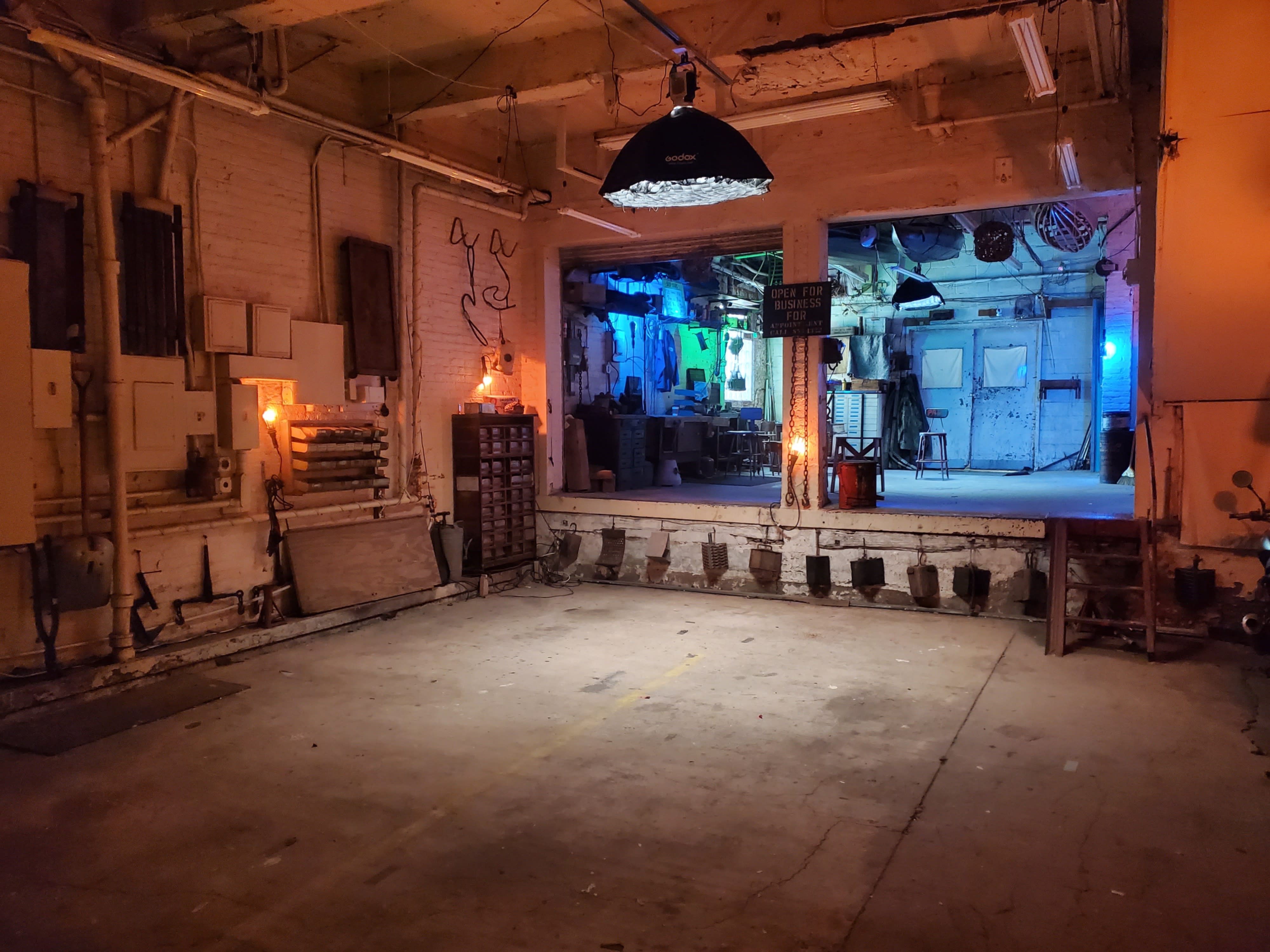 A drummer plays a red drum set in a dimly lit industrial space with amplifiers in the background.