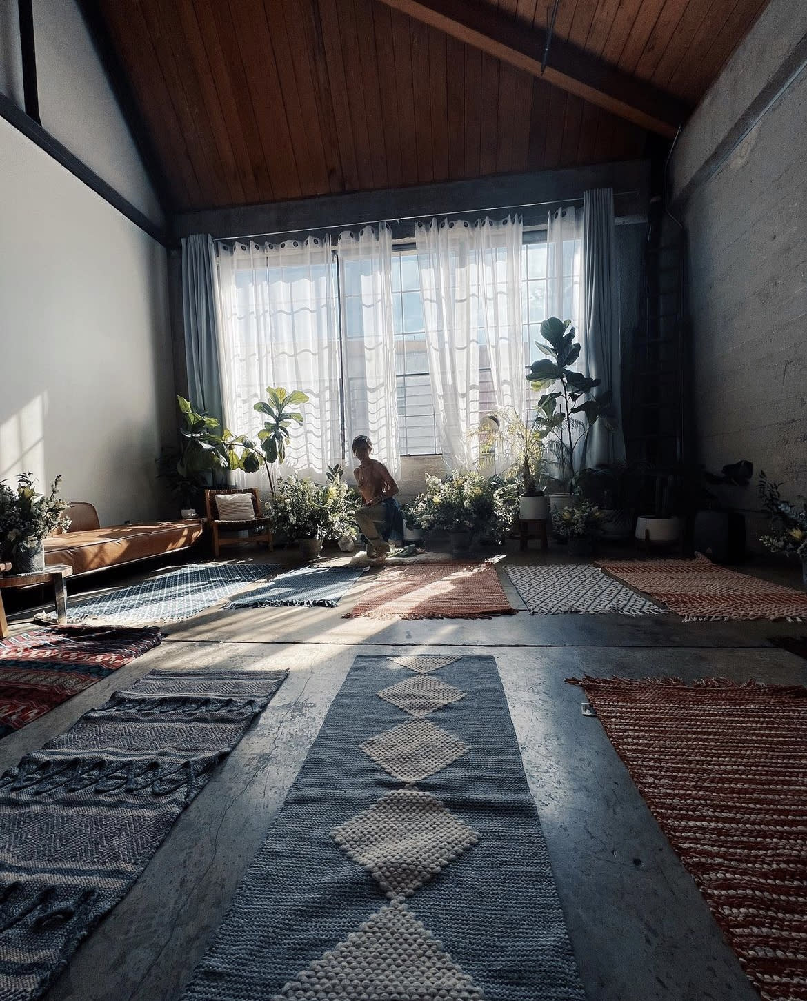 A group of four people sit together on a floor surrounded by plants, engaged in conversation.