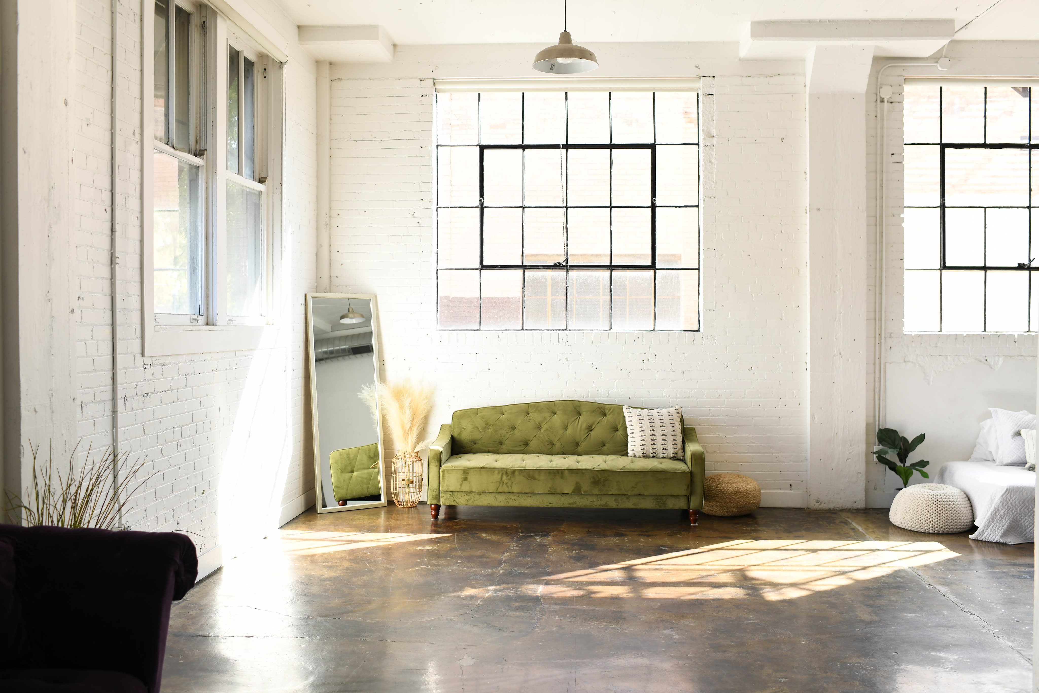 A woman in a floral dress sits on a yellow couch, enjoying the sunlight streaming in from a nearby window.