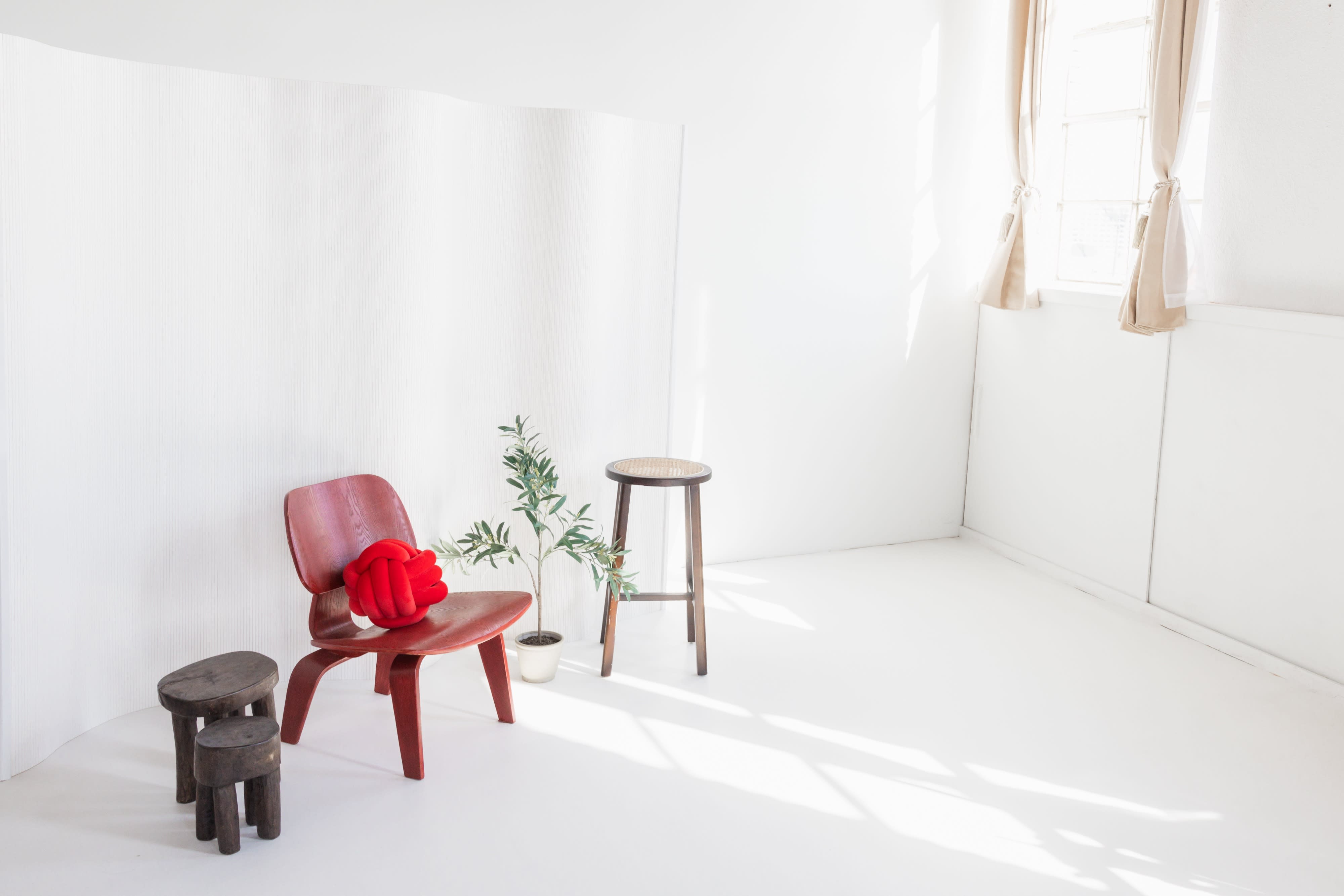A minimalistic photo shoot setup features a chair, a vase of flowers, and a textured rug in a well-lit studio.