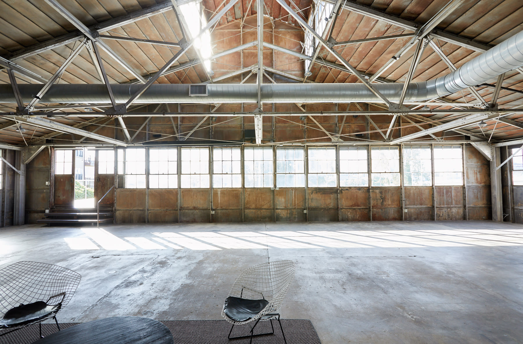 A group of dancers in vibrant outfits performs dynamic movements in an industrial space with large windows.