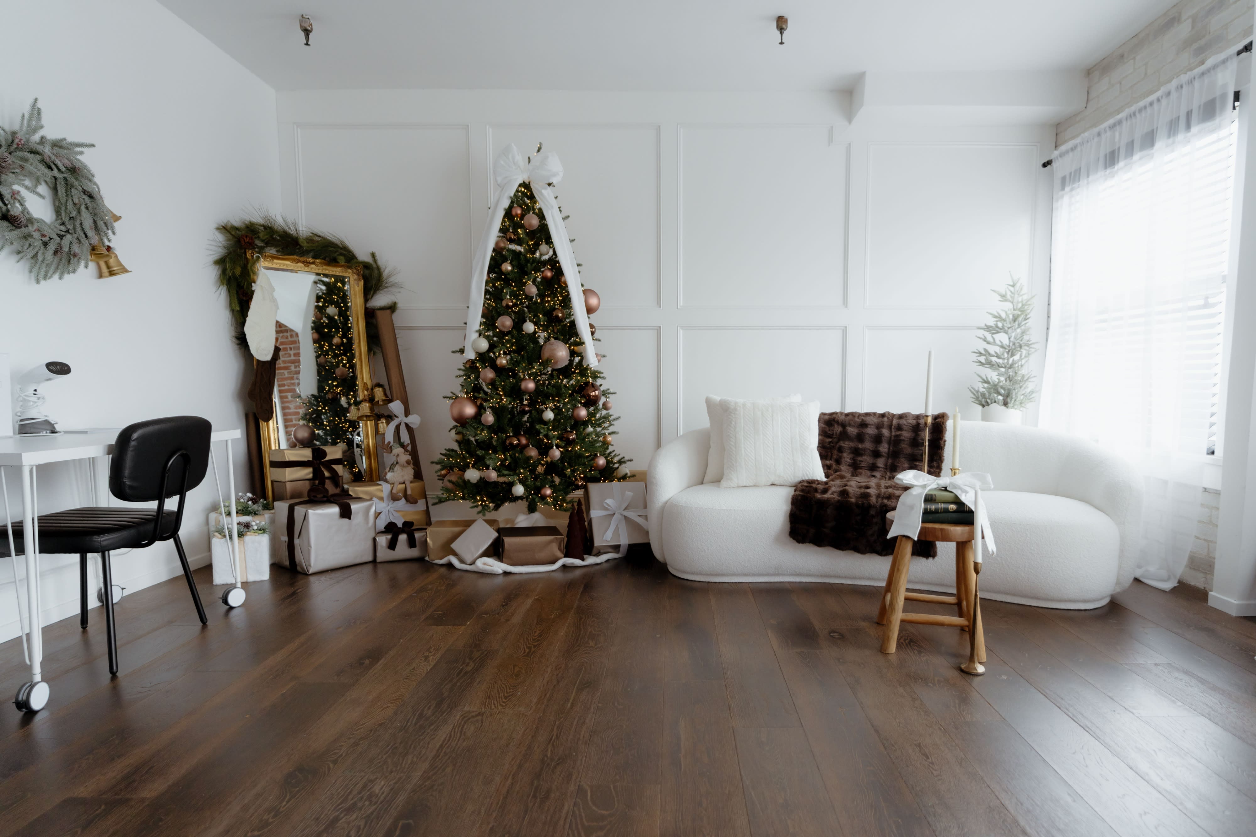 A photographer sets up a minimalistic studio scene featuring a white, curved couch against a light-colored wall, complemented by a mirror and a single decorative branch.