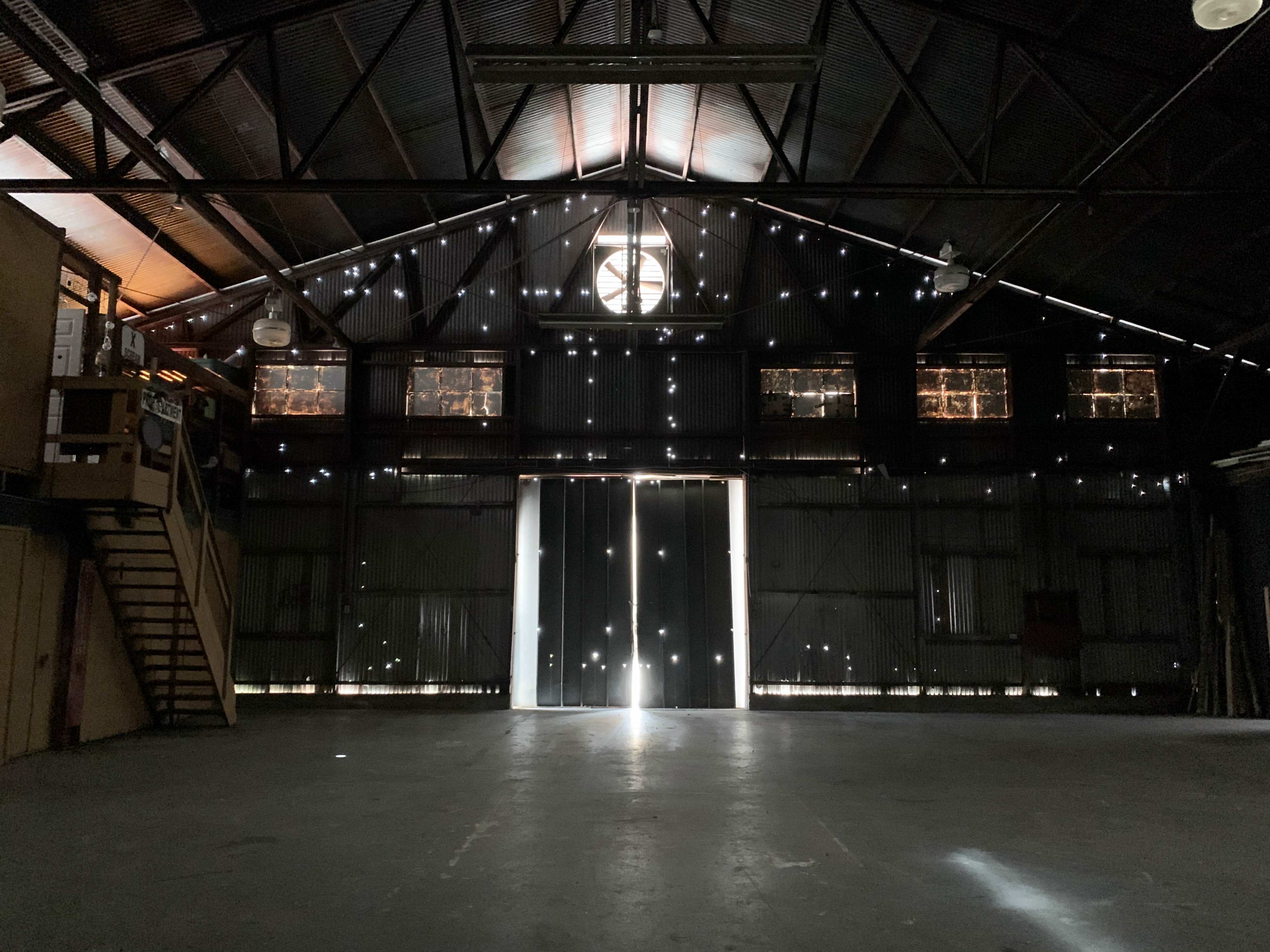 A small group of musicians stands in a smoke-filled warehouse, preparing for a live performance or rehearsal.