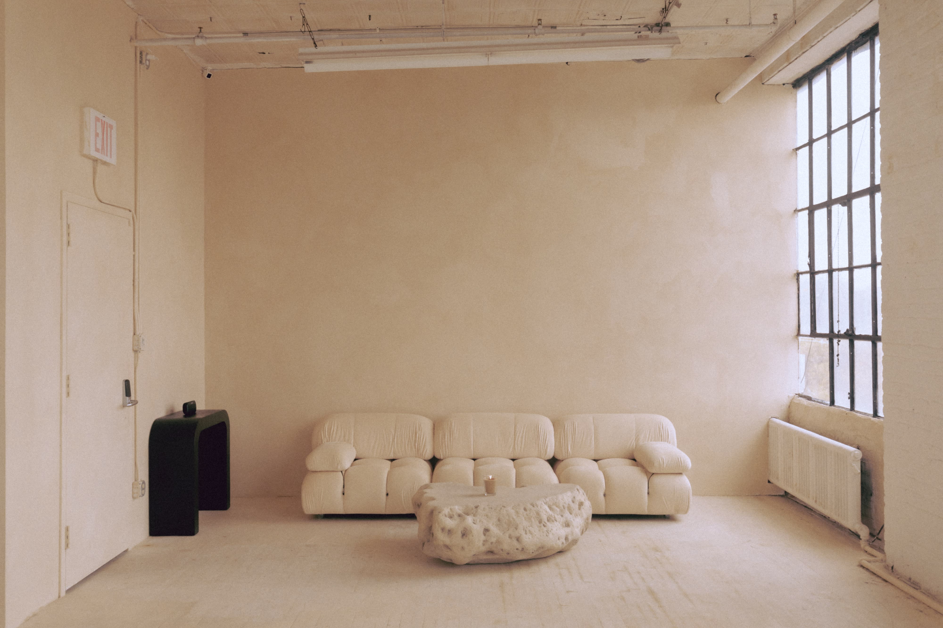A light-colored sofa is adorned with pink heart-shaped balloons, while a bottle of wine and two glasses sit on a stone coffee table in a minimalist space.