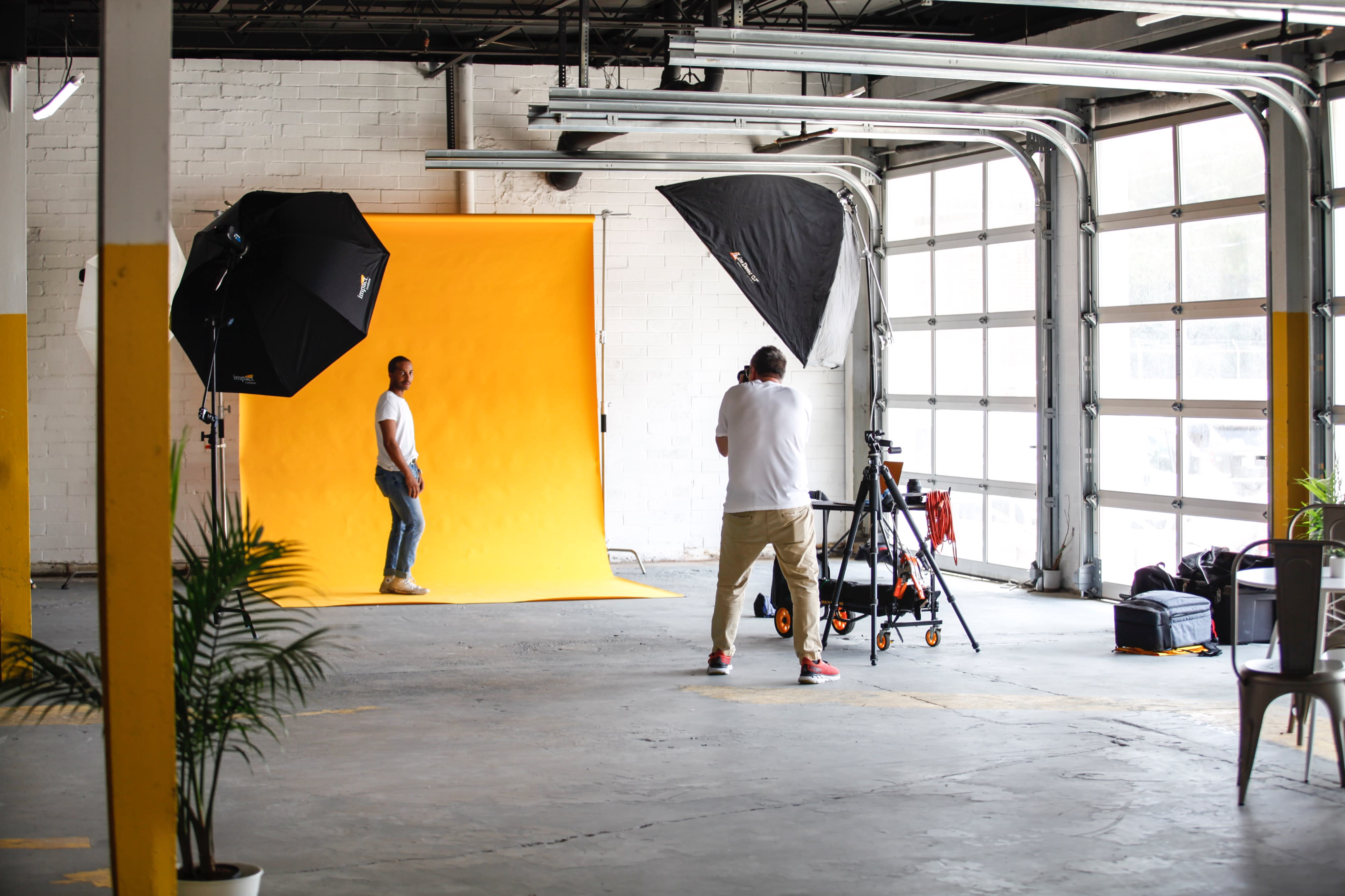 A man poses while another person captures the video in a studio setting with a white backdrop.