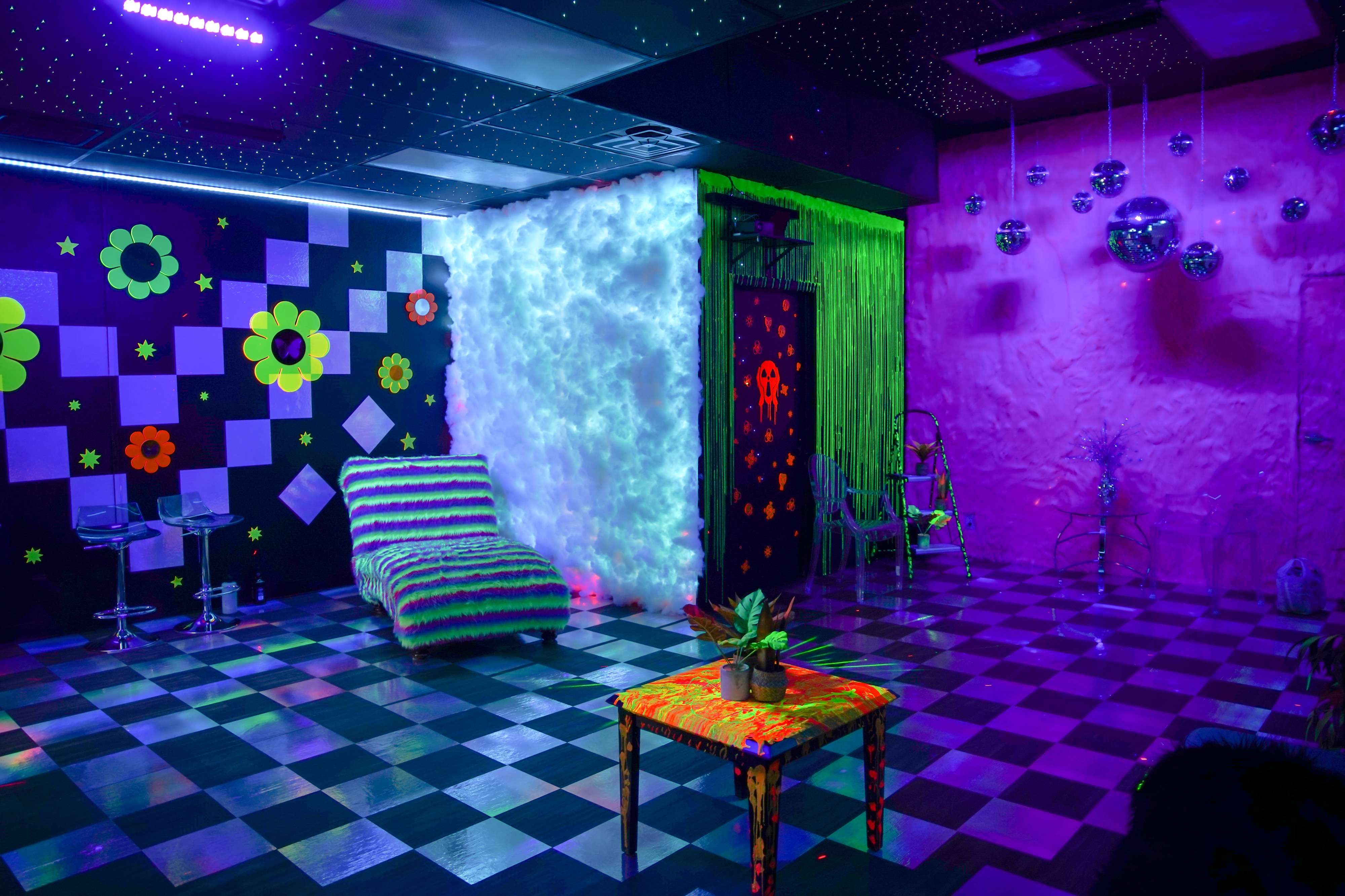 A colorful photoshoot setting features a checkerboard floor with vibrant wall decor and neon lighting.