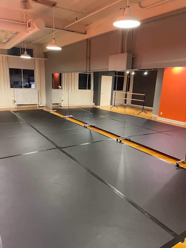 A woman performs a push-up while lifting one leg in a dance studio, with a mirror reflecting her movement.