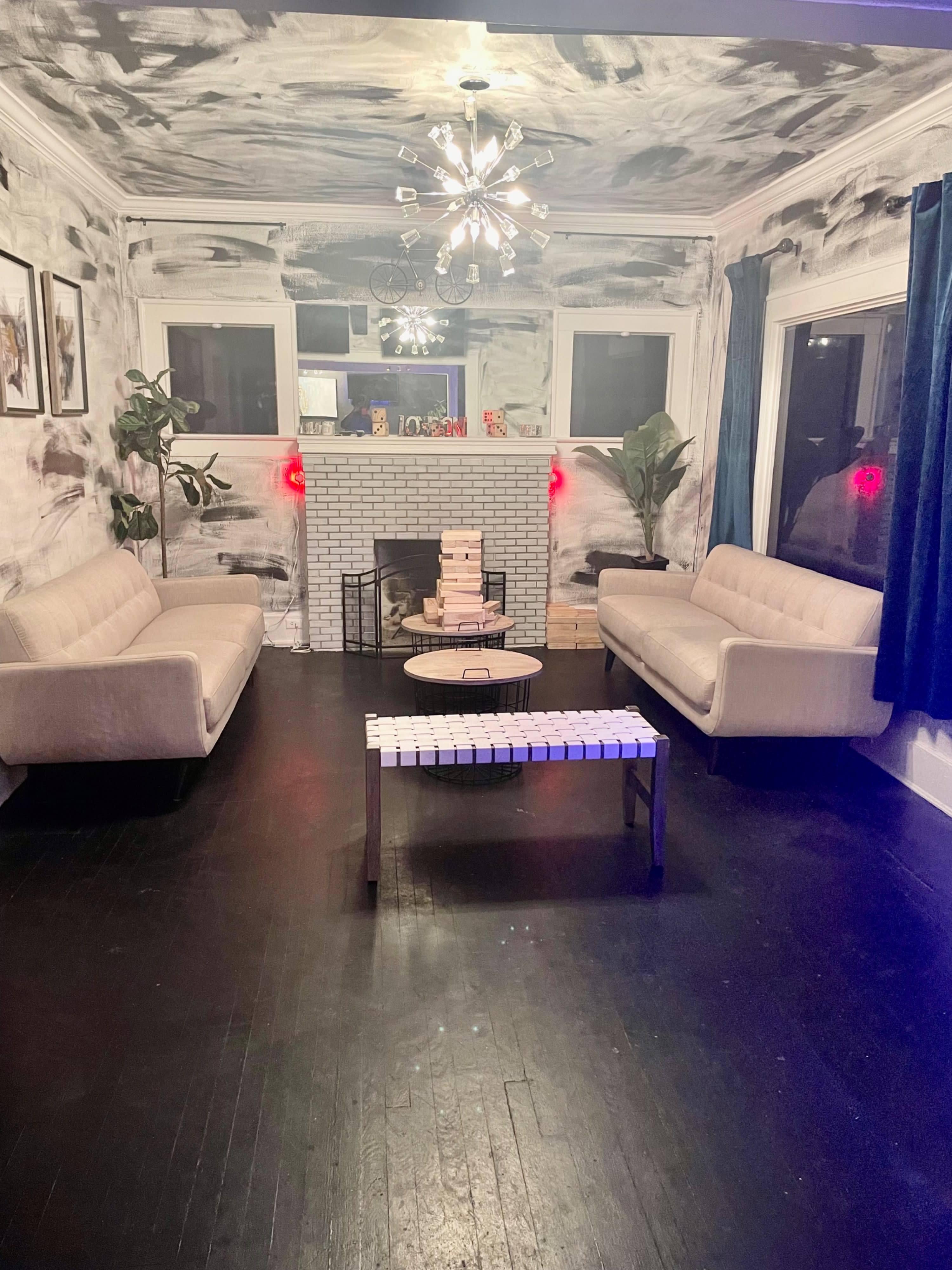 A young man proudly holds a tall stack of wooden blocks in a casually decorated room while another person sits on a couch in the background.