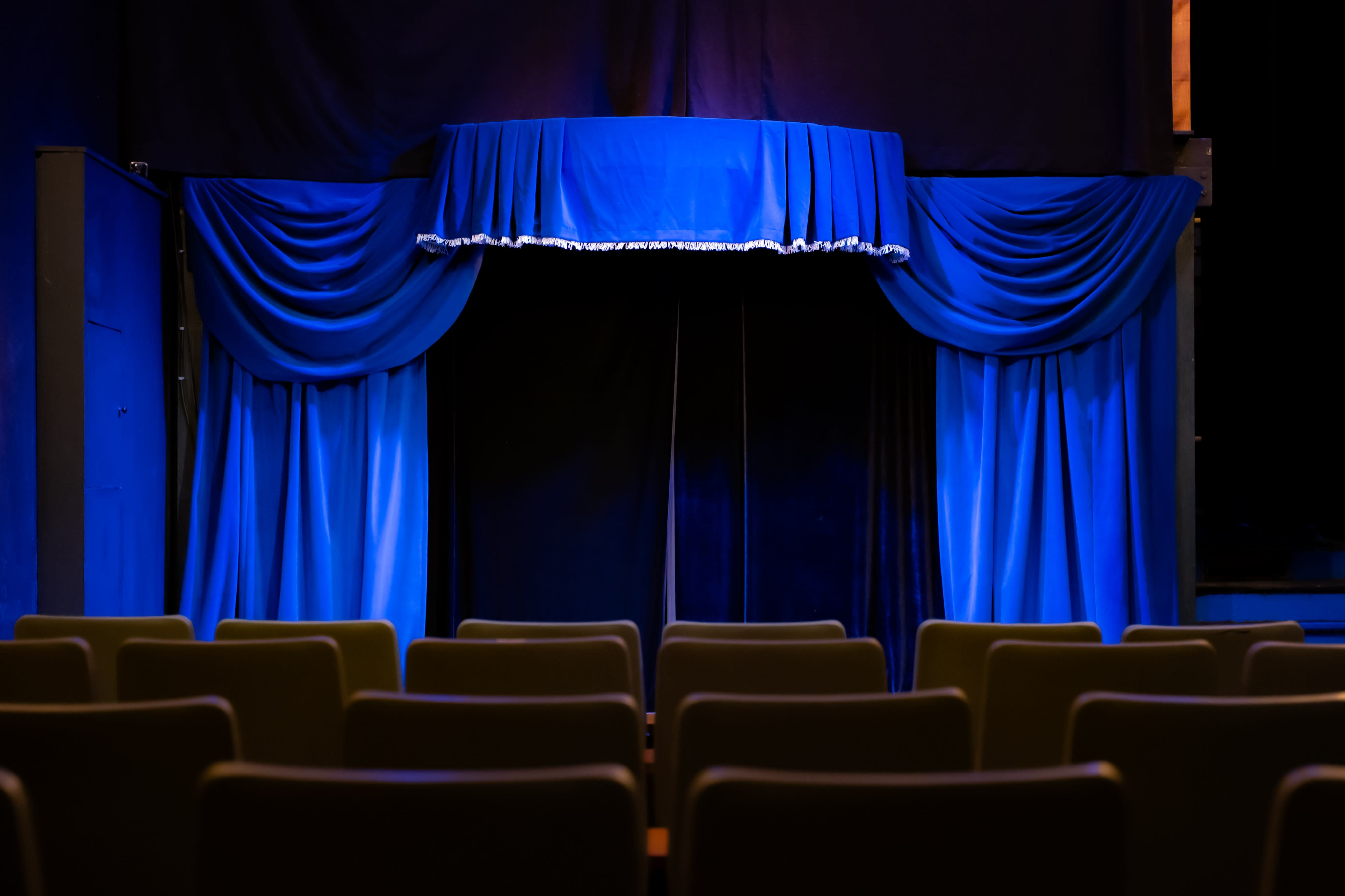 A video shoot is taking place on a stage with a performer in front of a microphone, while a camera captures the scene.