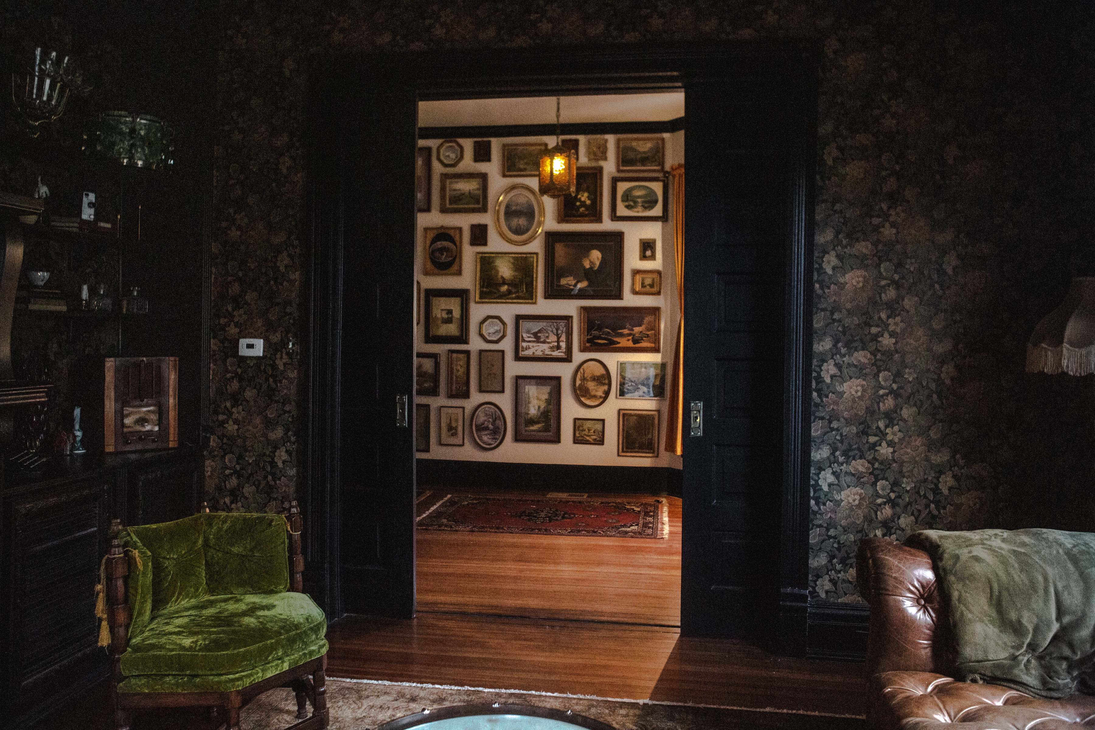 A plush leather sofa is positioned next to a vintage lamp illuminating a floral-patterned wall and a Christmas tree.