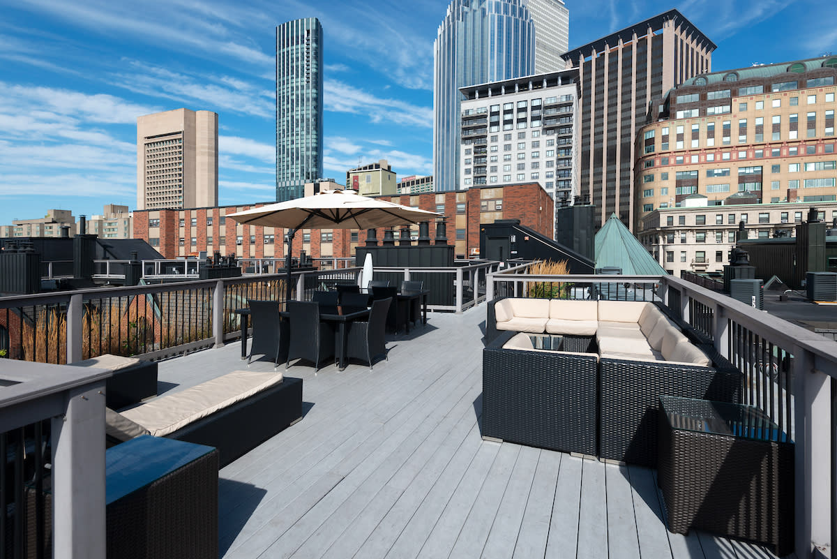 Four women pose together on a rooftop terrace with a city skyline in the background.