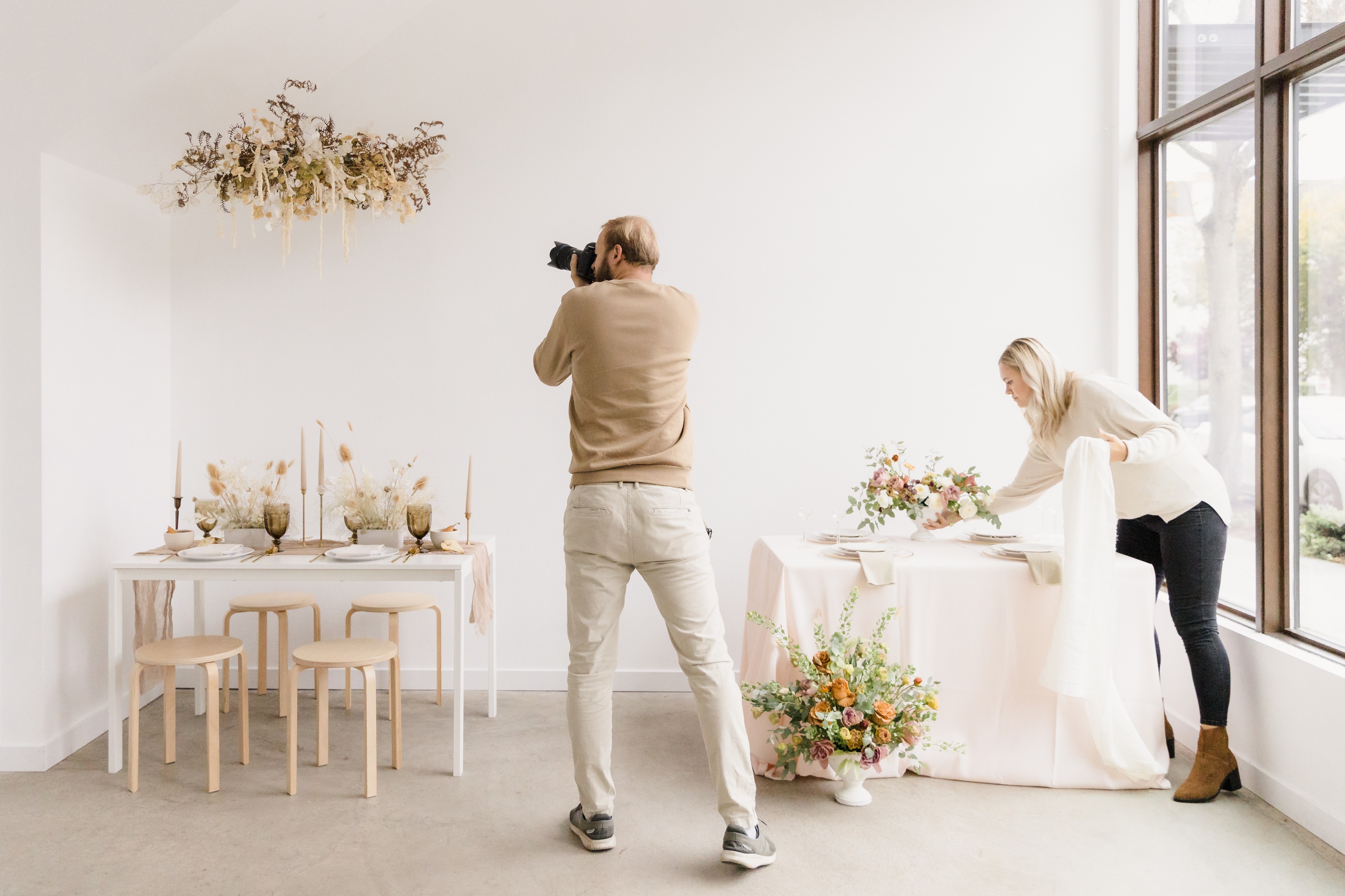Two brides sit at a decorated table, smiling and enjoying a photoshoot.