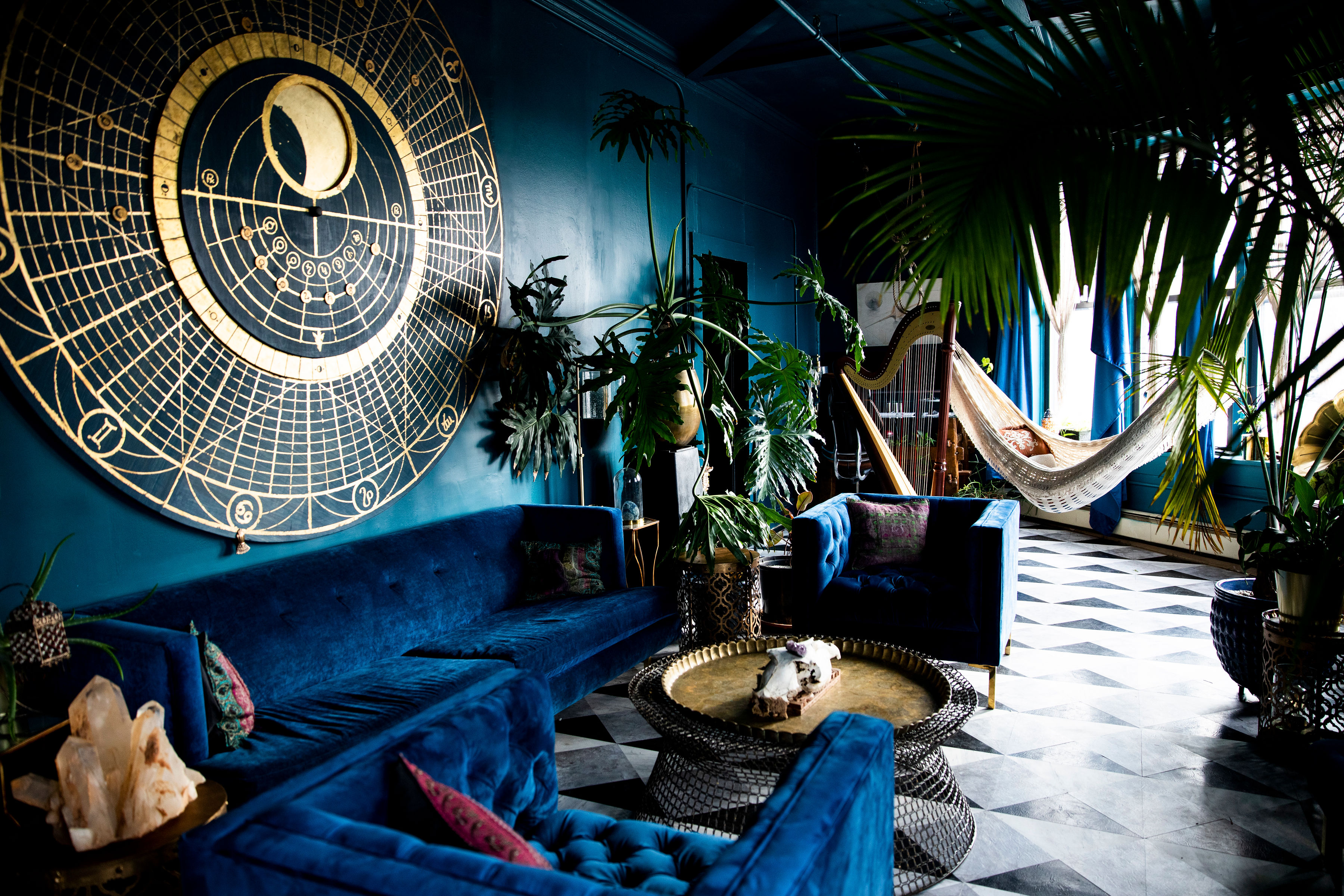 A music video shoot features a model in a white shirt seated on a blue couch against a large decorative backdrop.
